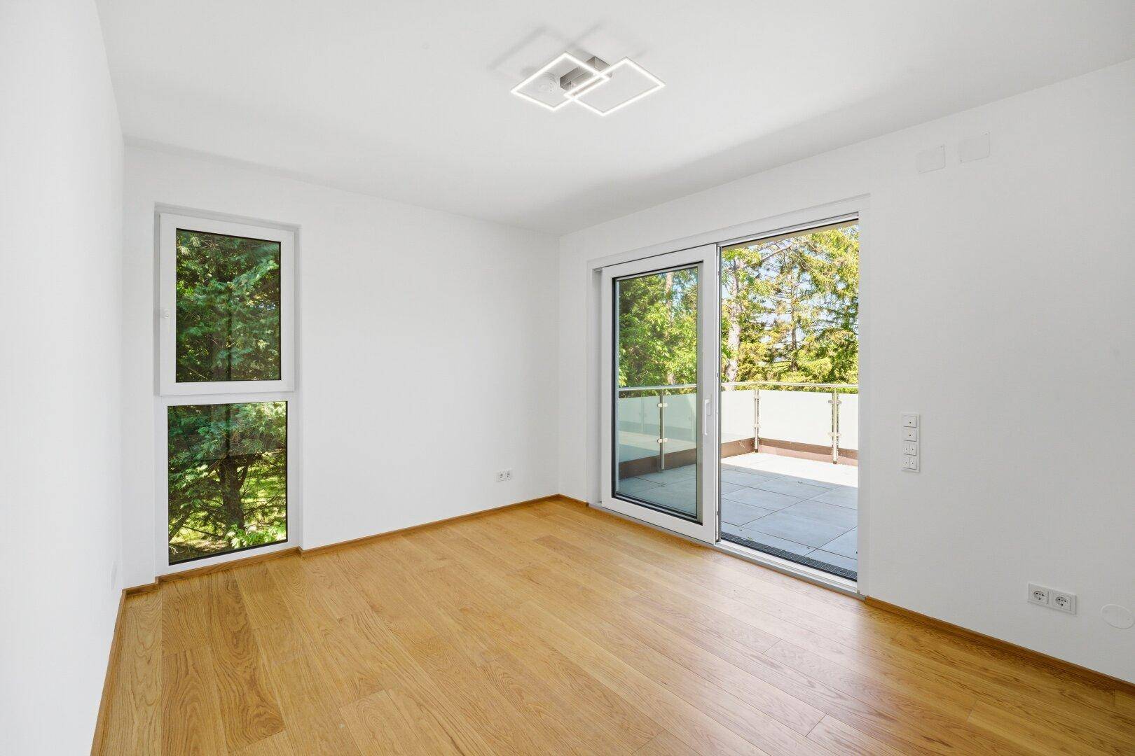 Helles Schlafzimmer mit Holzfußboden, großen Fenstern und direktem Zugang zu einer Terrasse.