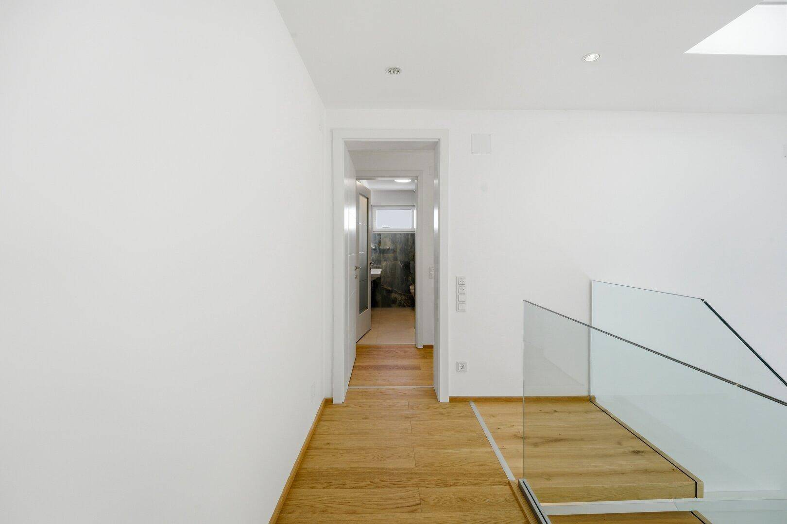 Heller Flur im Obergeschoss mit Holzfußboden und Zugang zu einem Badezimmer.