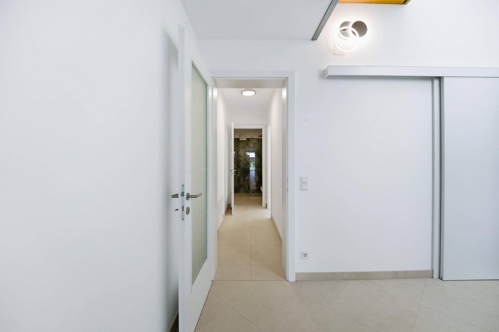 Heller Flur mit Fliesenboden und modernen Türen, der zu weiteren Räumen im Haus führt.