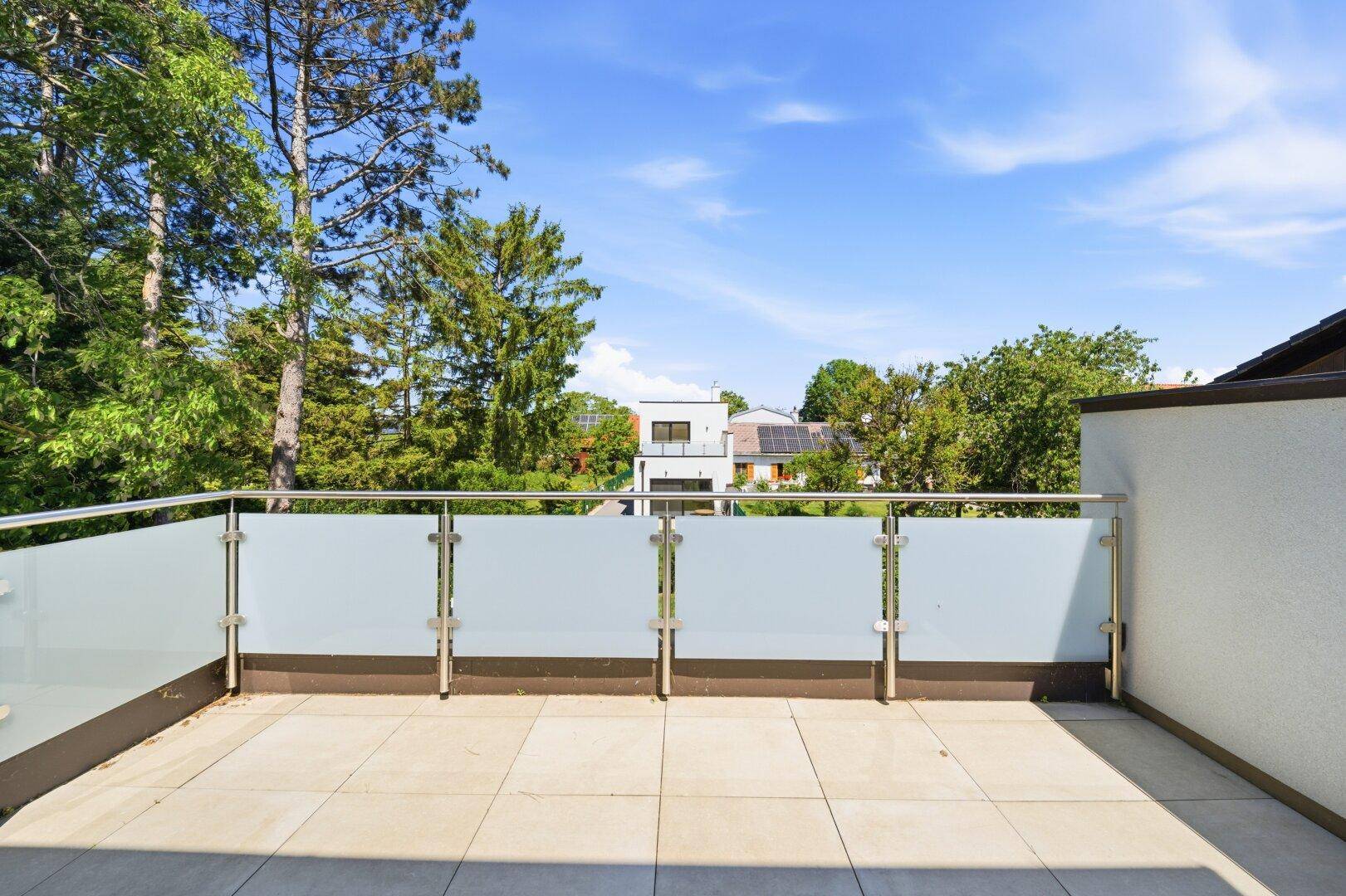 Große, sonnige Dachterrasse mit modernem Glasgeländer und Blick auf die umliegenden Häuser und Bäume.