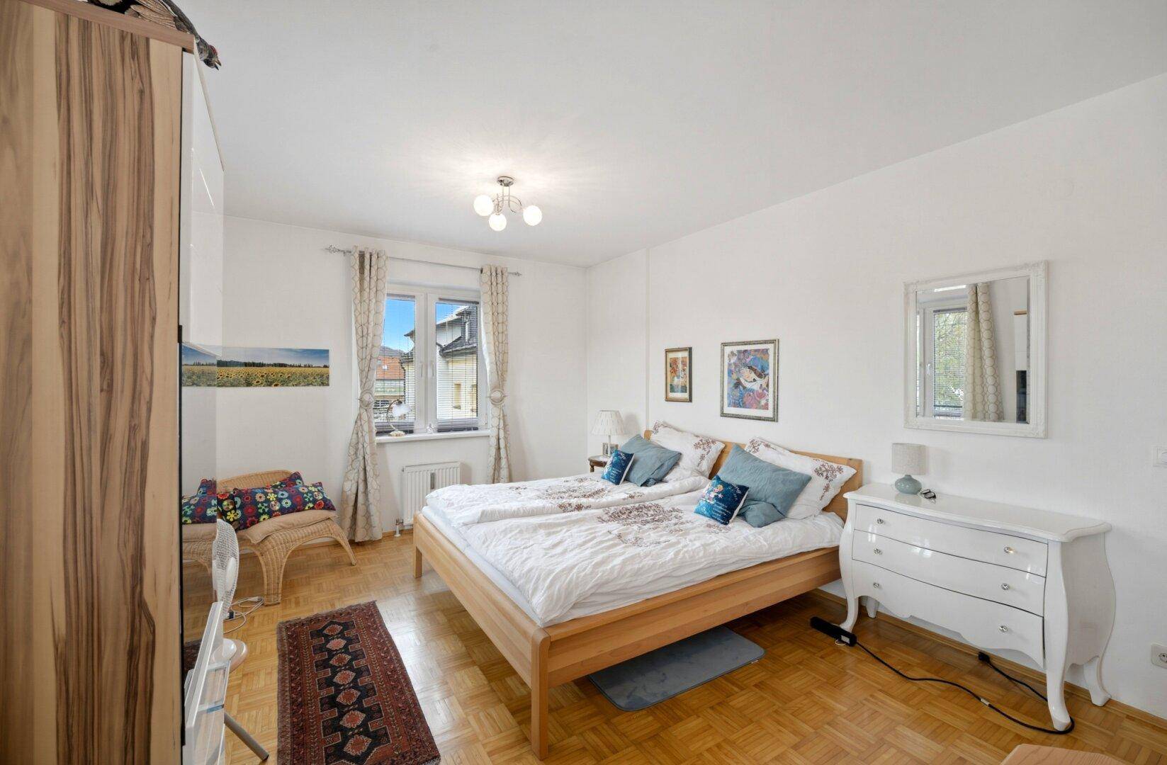 Gemütliches Schlafzimmer mit Parkettboden, hellem Holzdoppelbett und weißer Kommode.
