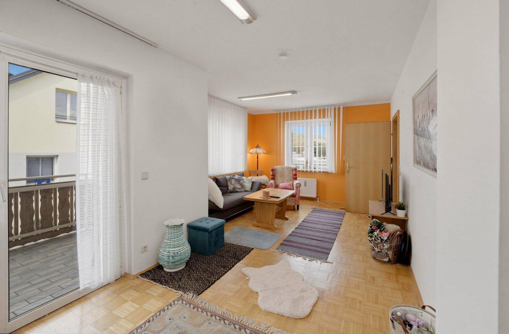 Wohnzimmer mit Parkettboden, orangefarbenen Wänden und Zugang zu einem Balkon.