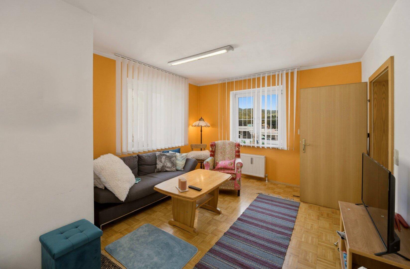 Helles Wohnzimmer mit Parkettboden, orangefarbenen Wänden und bequemen Sitzmöbeln.