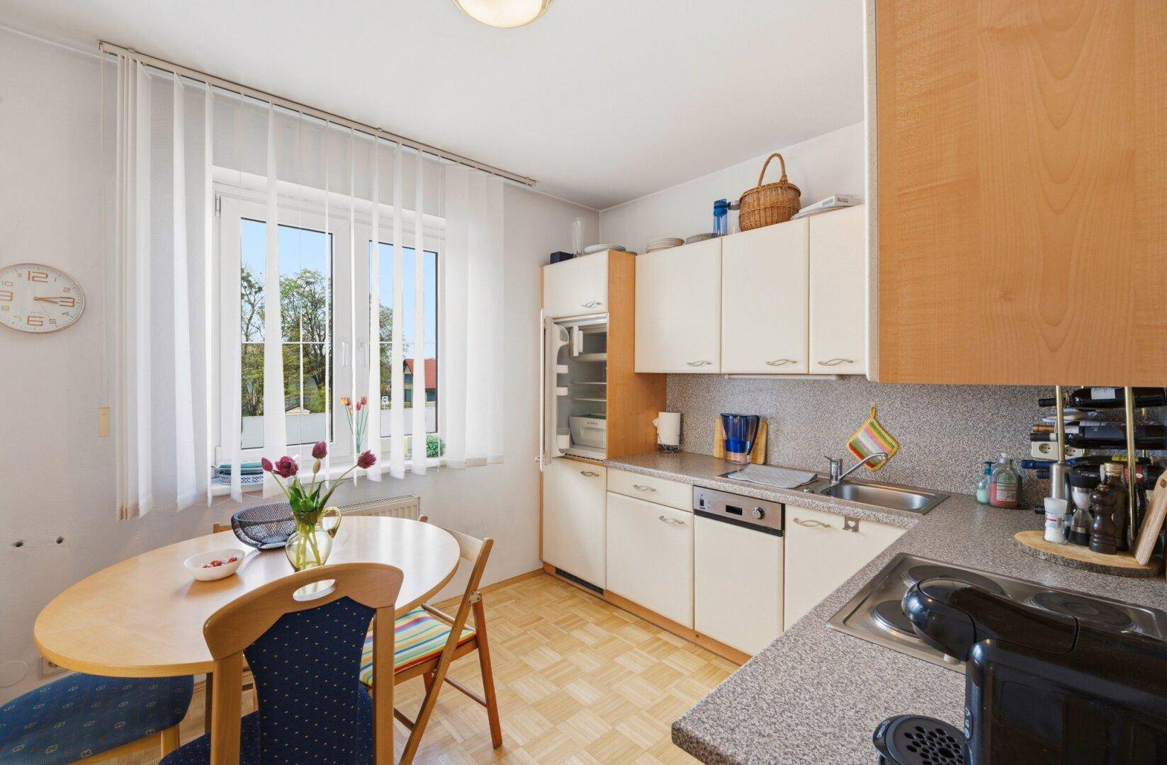 Funktionale Küche mit hellen Schränken, Esstisch und Fenster mit Blick ins Freie.