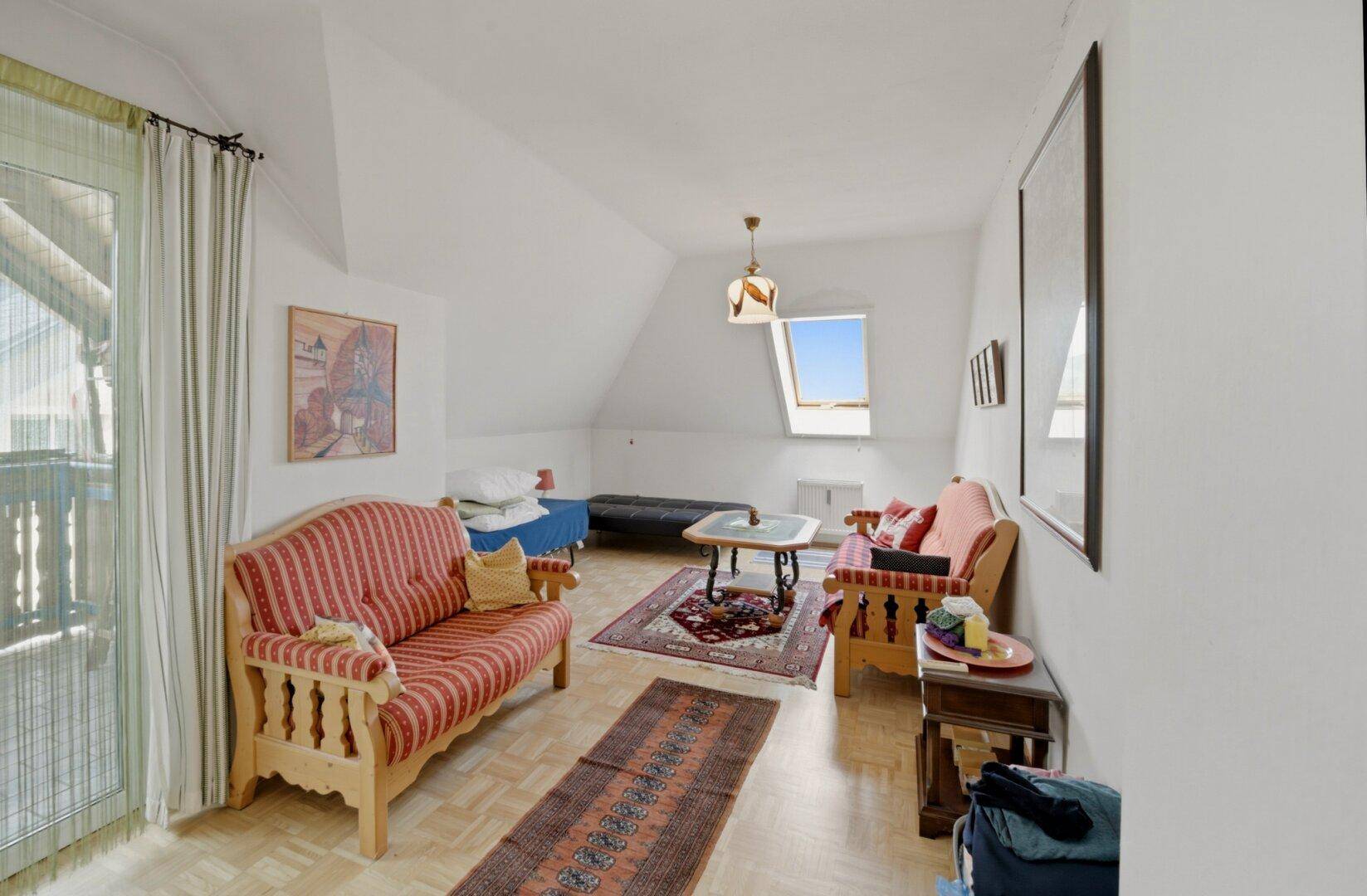 Gemütliches Wohnzimmer im Dachgeschoss mit Schrägen, Parkettboden und Zugang zum Balkon.