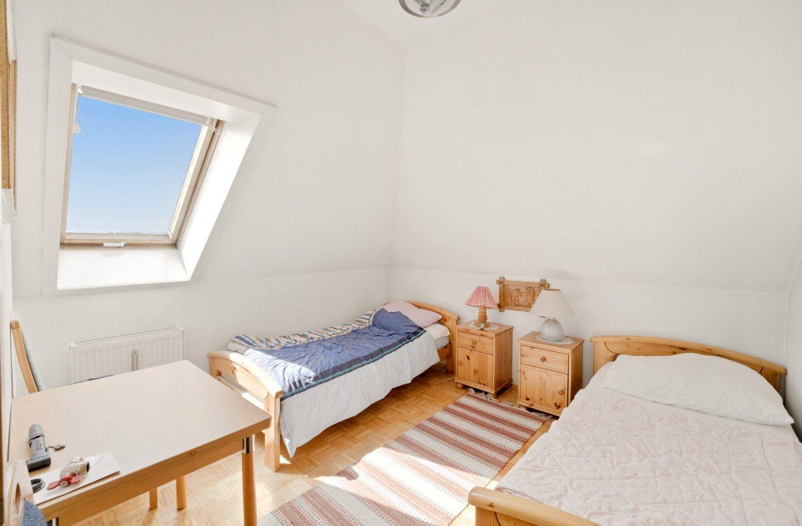 Helles Schlafzimmer im Dachgeschoss mit zwei Einzelbetten, Parkettboden und Dachfenster.