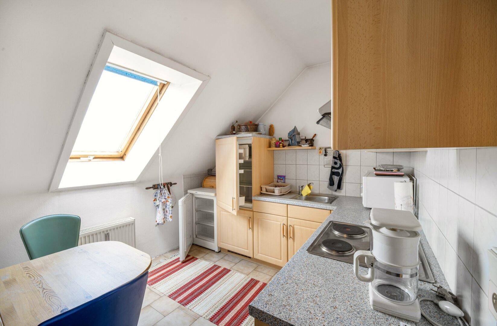 Kleine Küchenzeile im Dachgeschoss mit Dachfenster, Kochfeld und Kühlschrank.