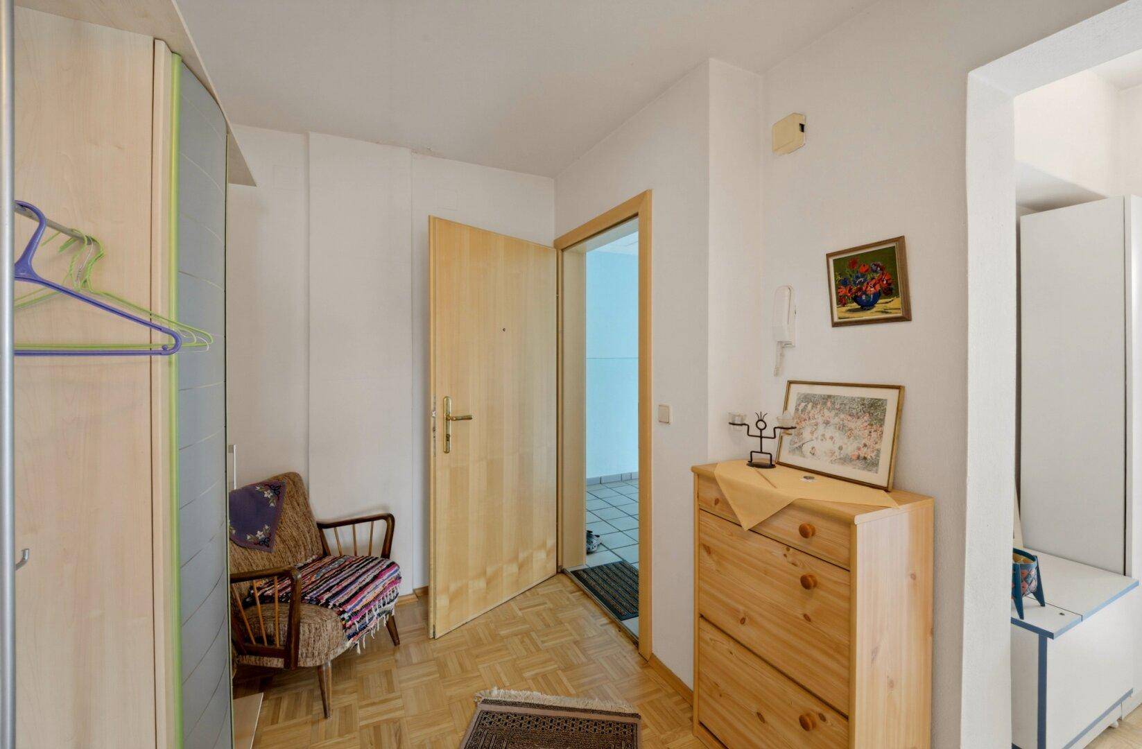 Eingangsbereich mit Parkettboden, Holzkommode und Garderobe, hell und einladend.