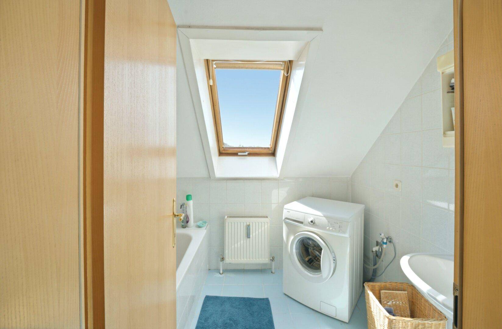 Badezimmer im Dachgeschoss mit Waschmaschine, Badewanne und Dachfenster für natürliches Licht.