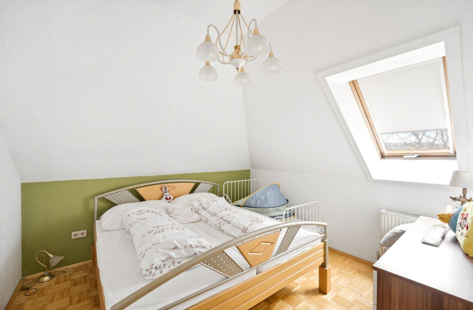 Helles Schlafzimmer im Dachgeschoss mit Einzelbett, Parkettboden und Dachfenster.