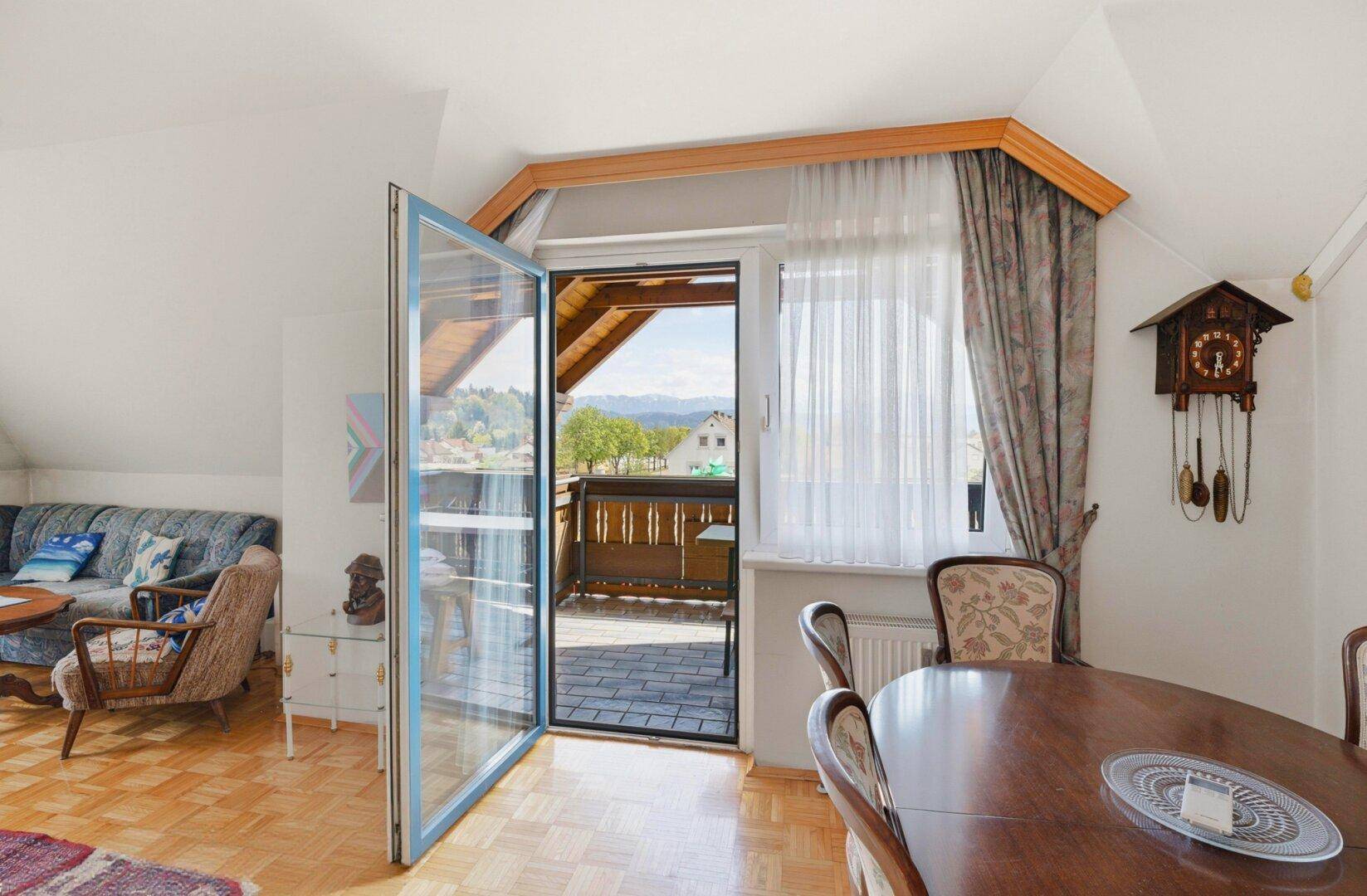 Helles Wohn- und Esszimmer mit Parkettboden, Zugang zum Balkon und Bergblick.