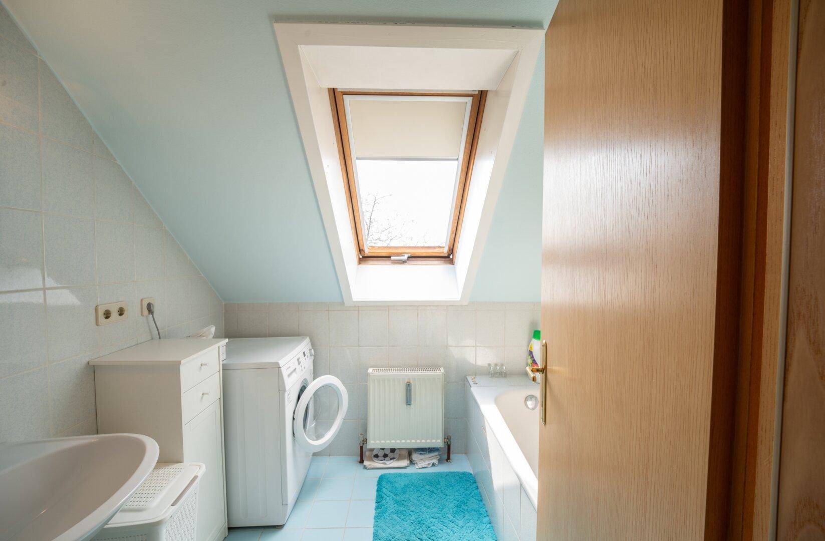 Badezimmer im Dachgeschoss mit Badewanne, Waschmaschine und Dachfenster für natürliches Licht.