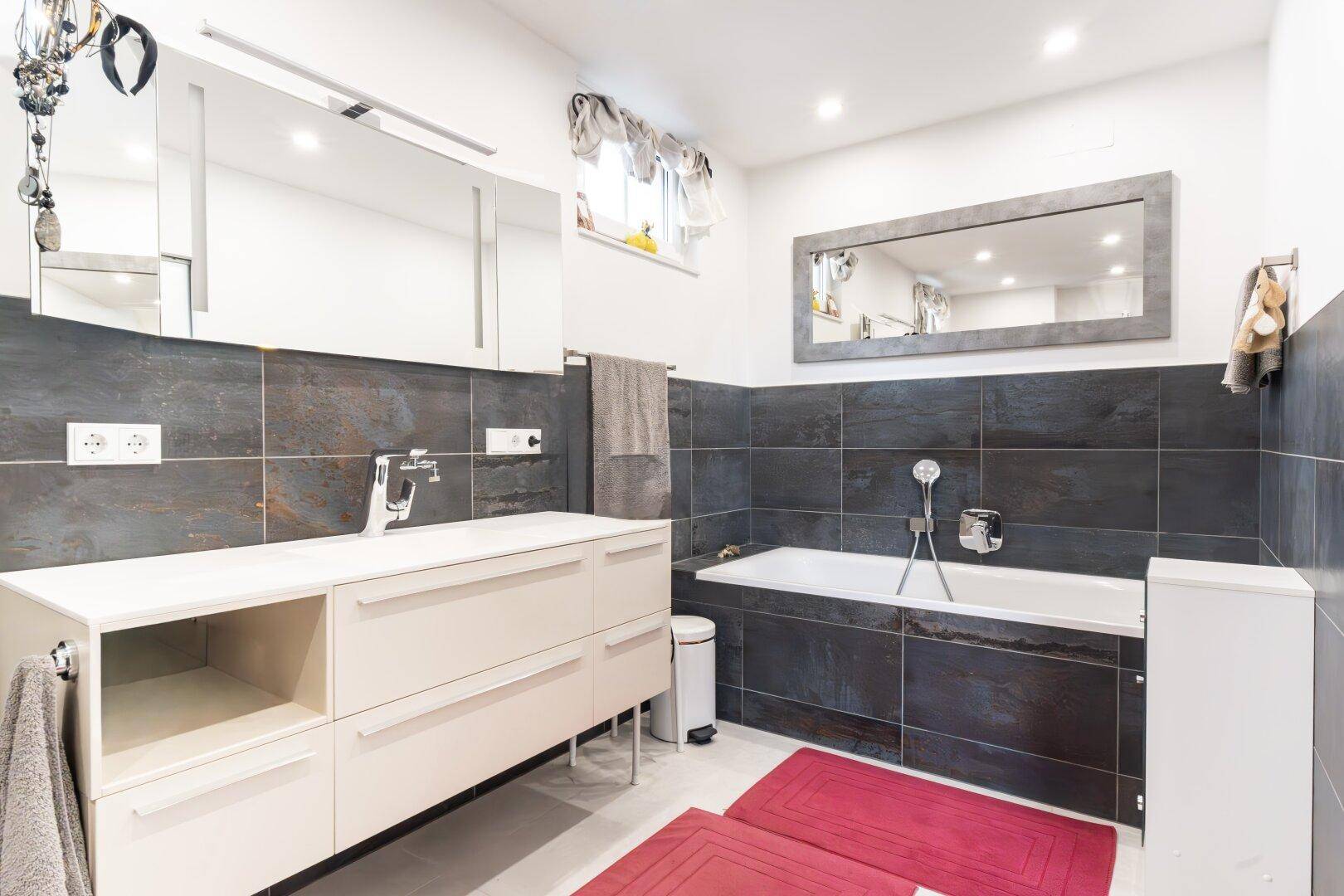 Elegantes Badezimmer mit Badewanne, großem Waschtisch und Spiegelschränken, hell und geräumig.