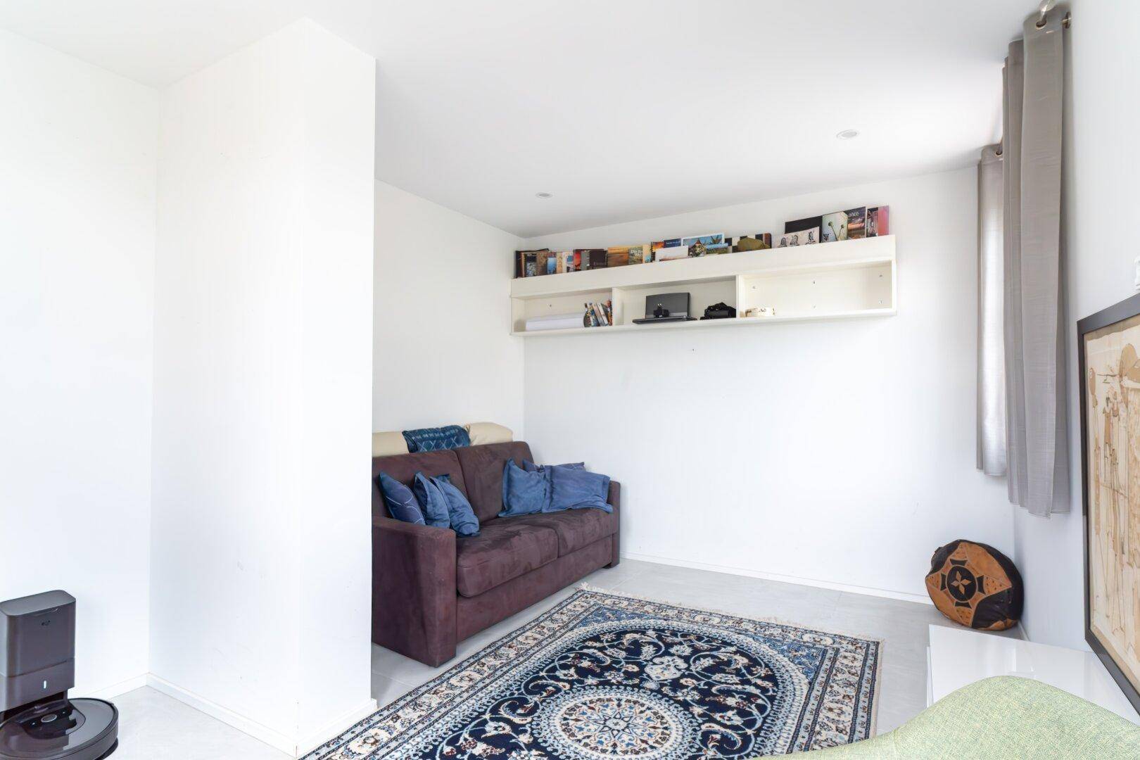 Heller Raum mit Sofa, Teppich und Bücherregal, ideal als gemütlicher Rückzugsort oder Arbeitszimmer.