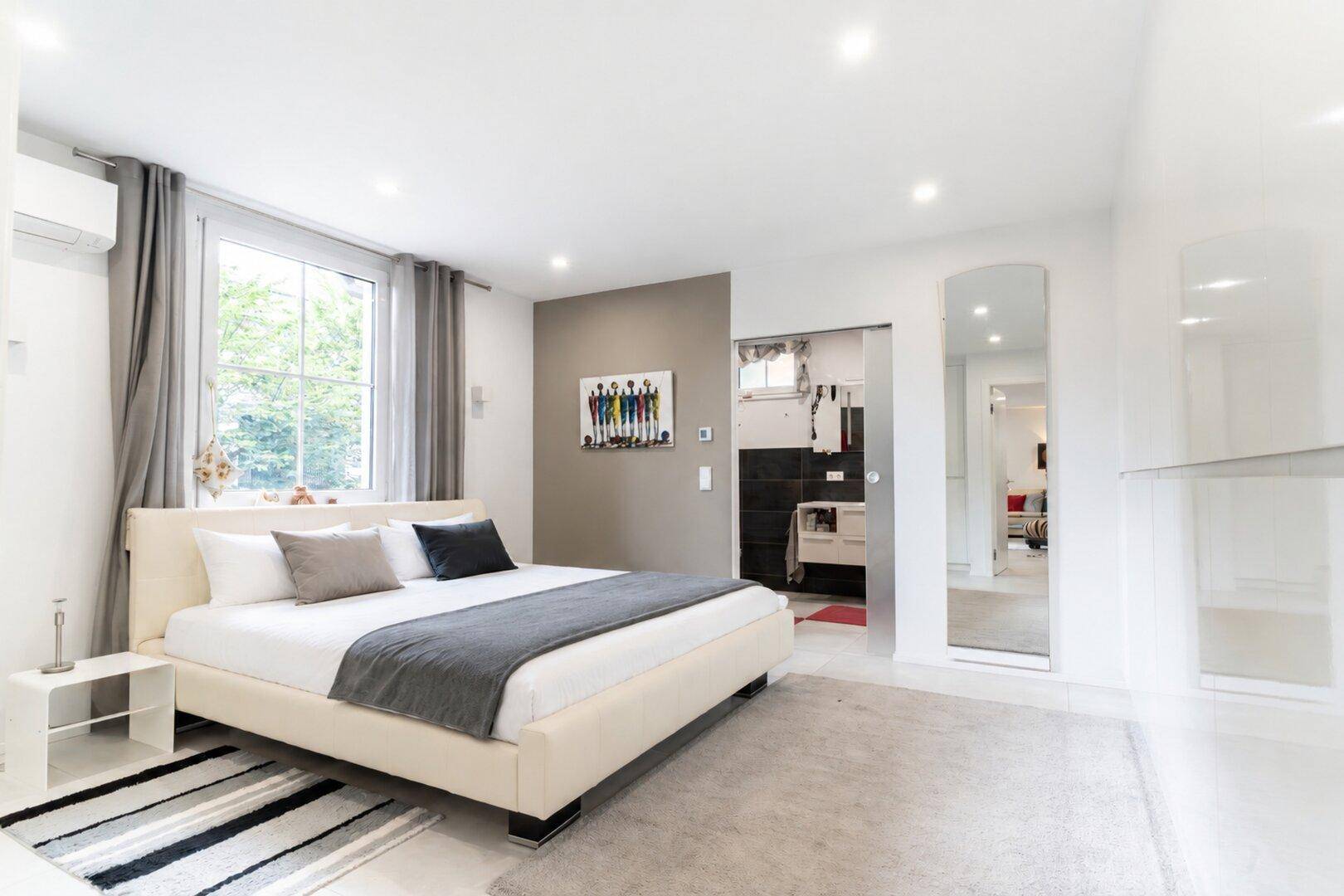 Helles Schlafzimmer mit Doppelbett, Klimaanlage und Zugang zu einem modernen Badezimmer.