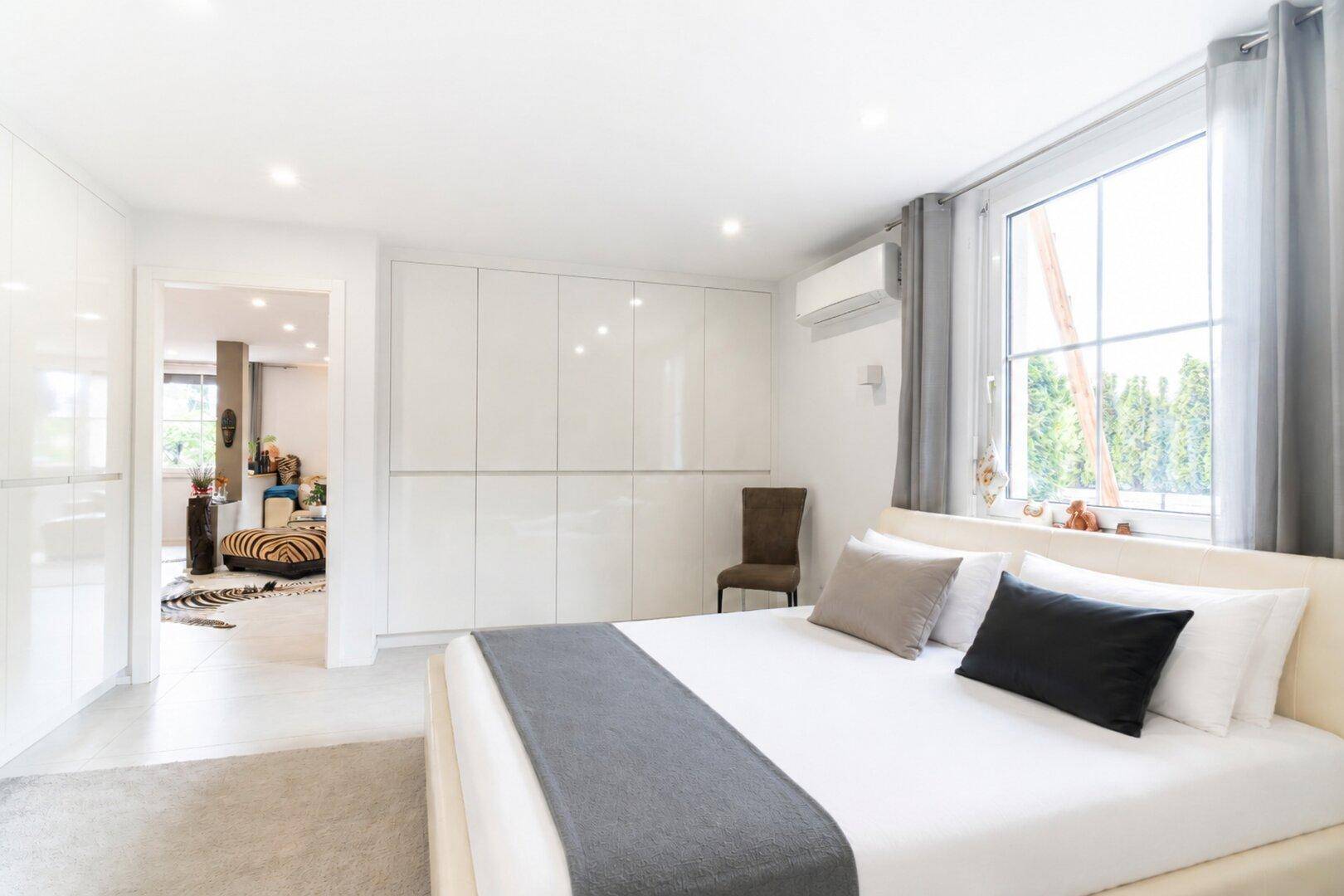Modernes Schlafzimmer mit großem Bett, Einbauschränken und viel Tageslicht durch das Fenster.
