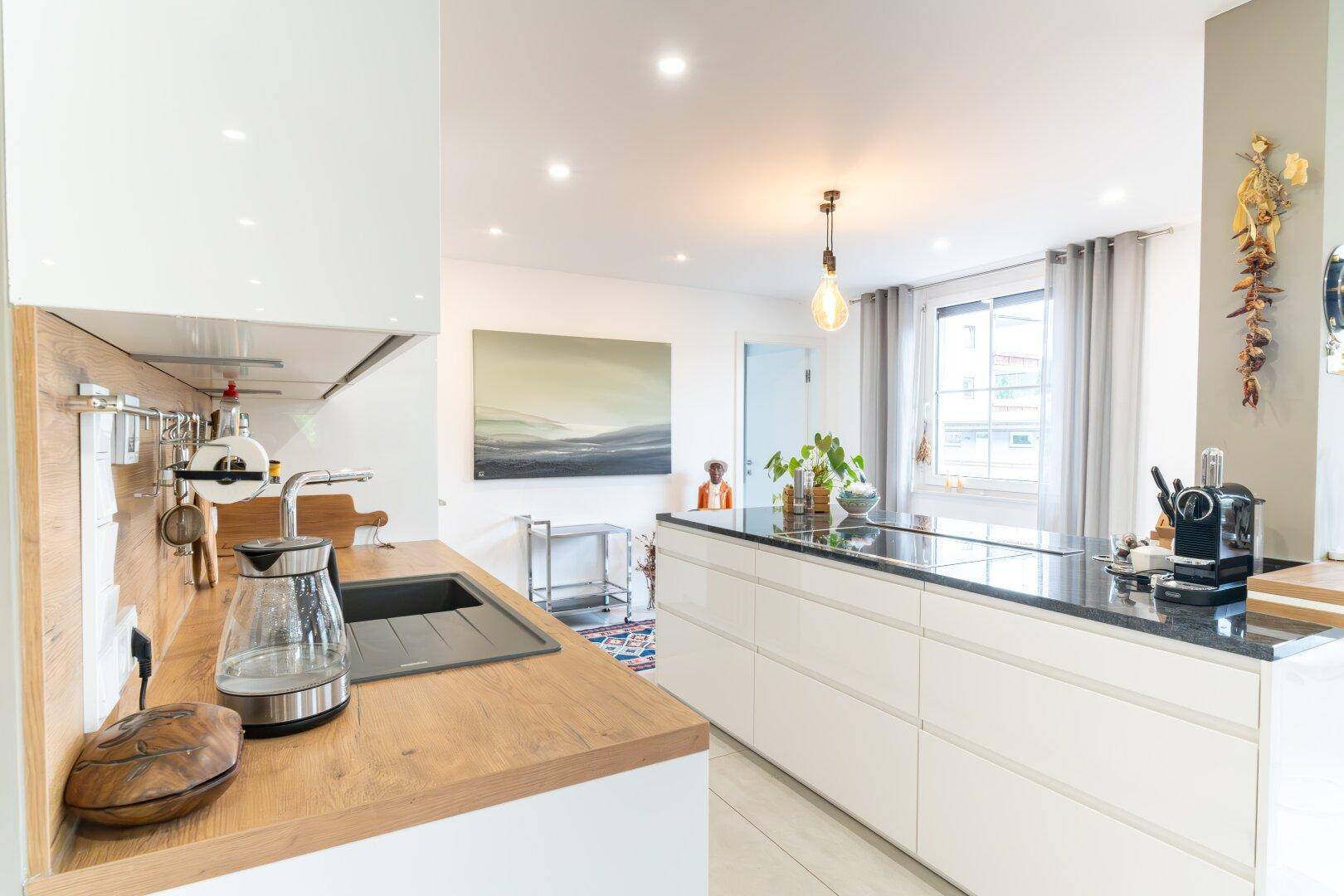 Moderne Küche mit weißer Hochglanzfront, Holzdetails und dunkler Kücheninsel, offen zum Wohnbereich.
