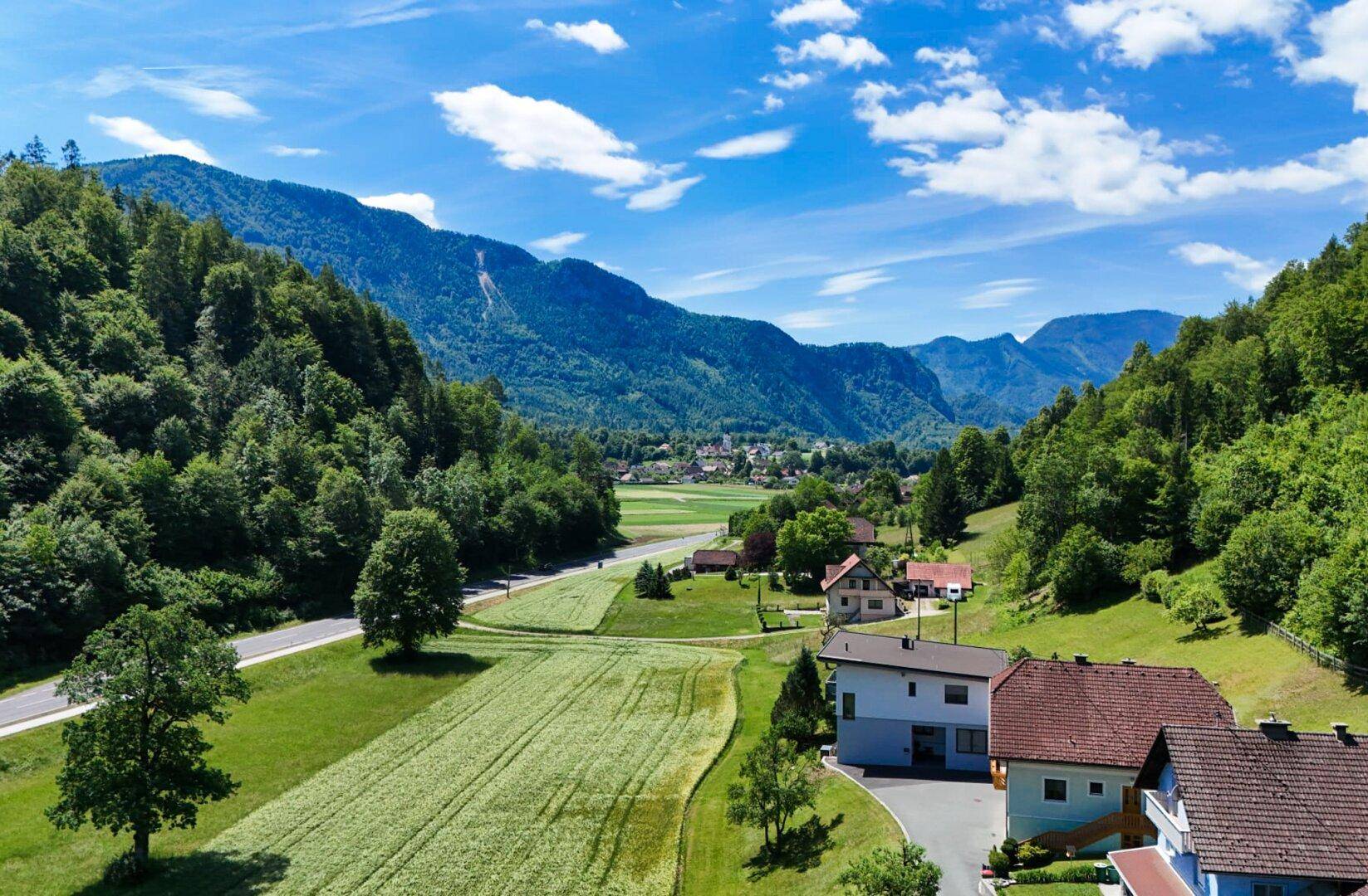 Malerische Landschaft mit Häusern, Feldern und Bergen unter einem strahlend blauen Himmel.