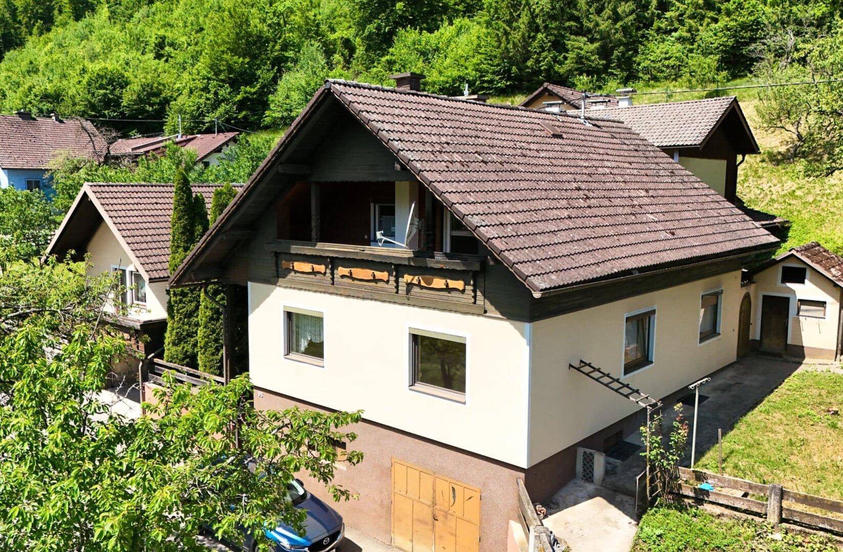 Traditionelles Wohnhaus mit braunem Ziegeldach und Holzbalkon, eingebettet in grüne Natur.