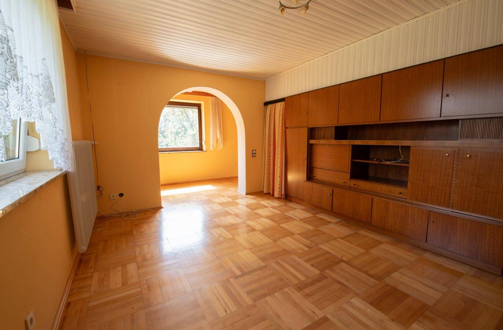 Wohnzimmer mit Parkettboden, Holzwandelementen und einem Bogen zu einem weiteren Raum.