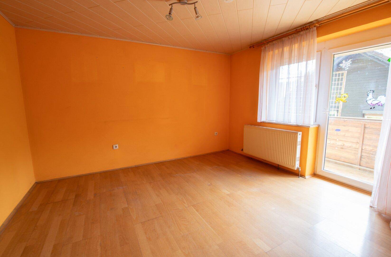 Heller Raum mit orangefarbenen Wänden, Holzboden und Zugang zu einem Balkon.