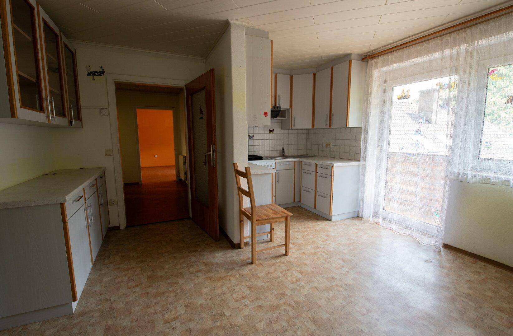 Einfache Küche mit weißen Schränken, Fliesen und einem Fenster mit Blick nach draußen.