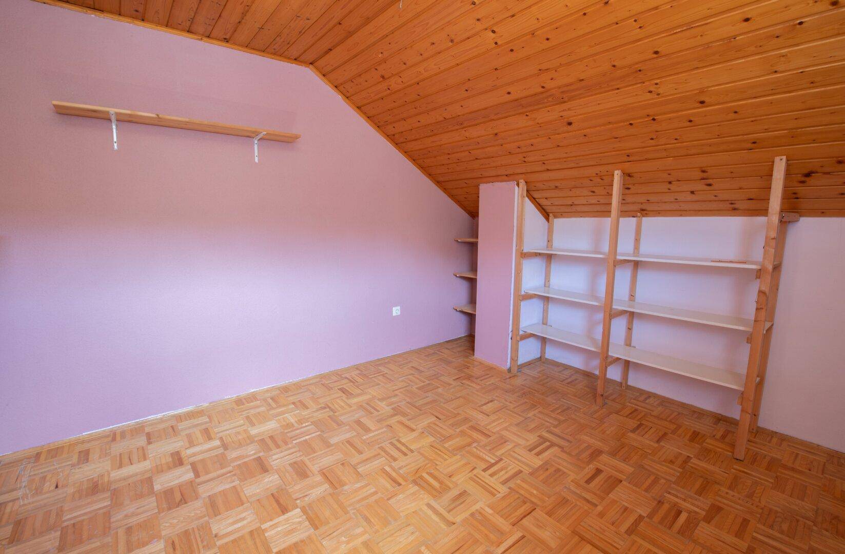 Dachzimmer mit Holzdecke, schrägen Wänden und eingebauten Regalen, bereit zur individuellen Gestaltung.