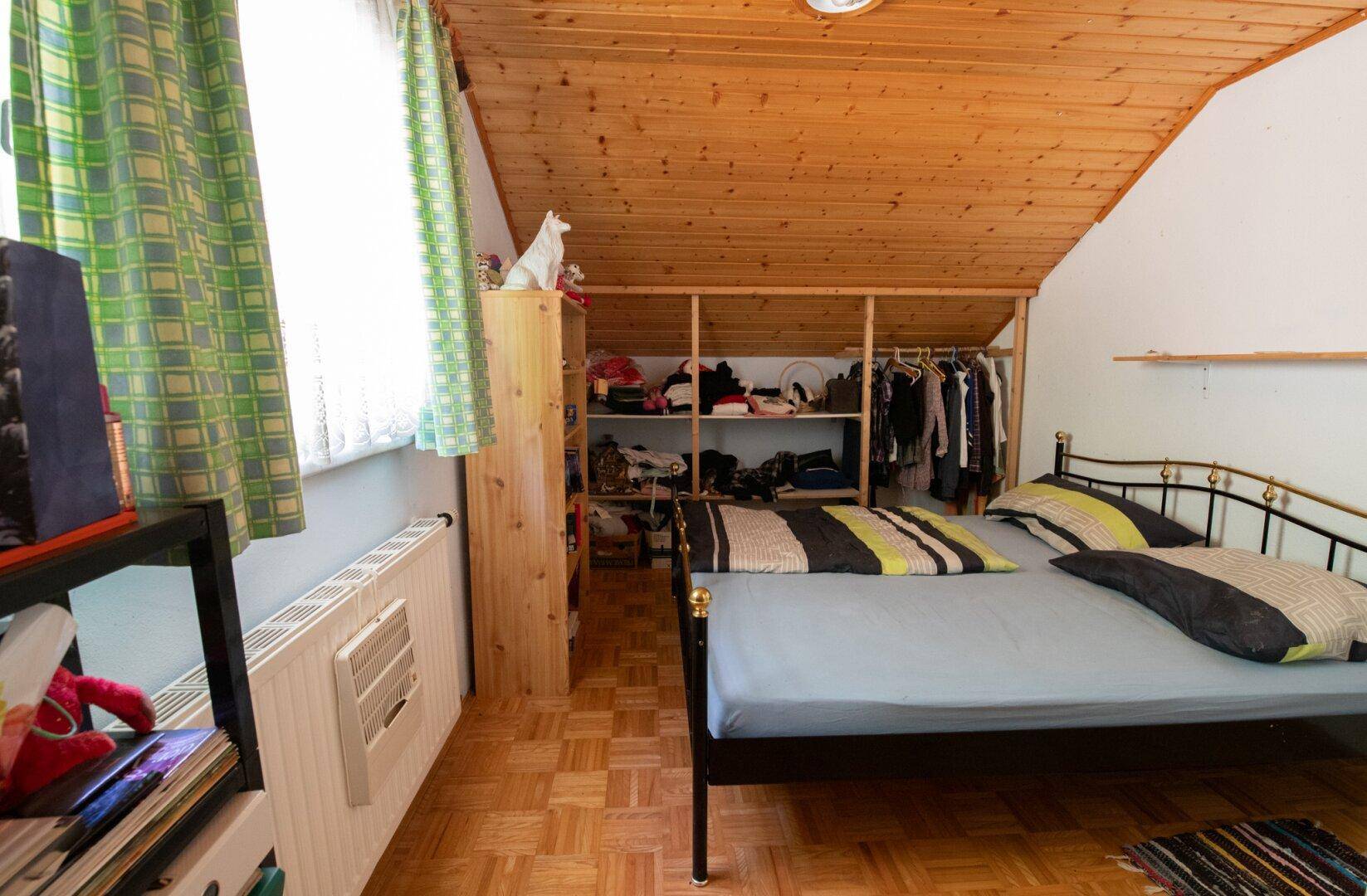 Gemütliches Schlafzimmer im Dachgeschoss mit Holzdecke, Parkettboden und offenem Kleiderschrankbereich.