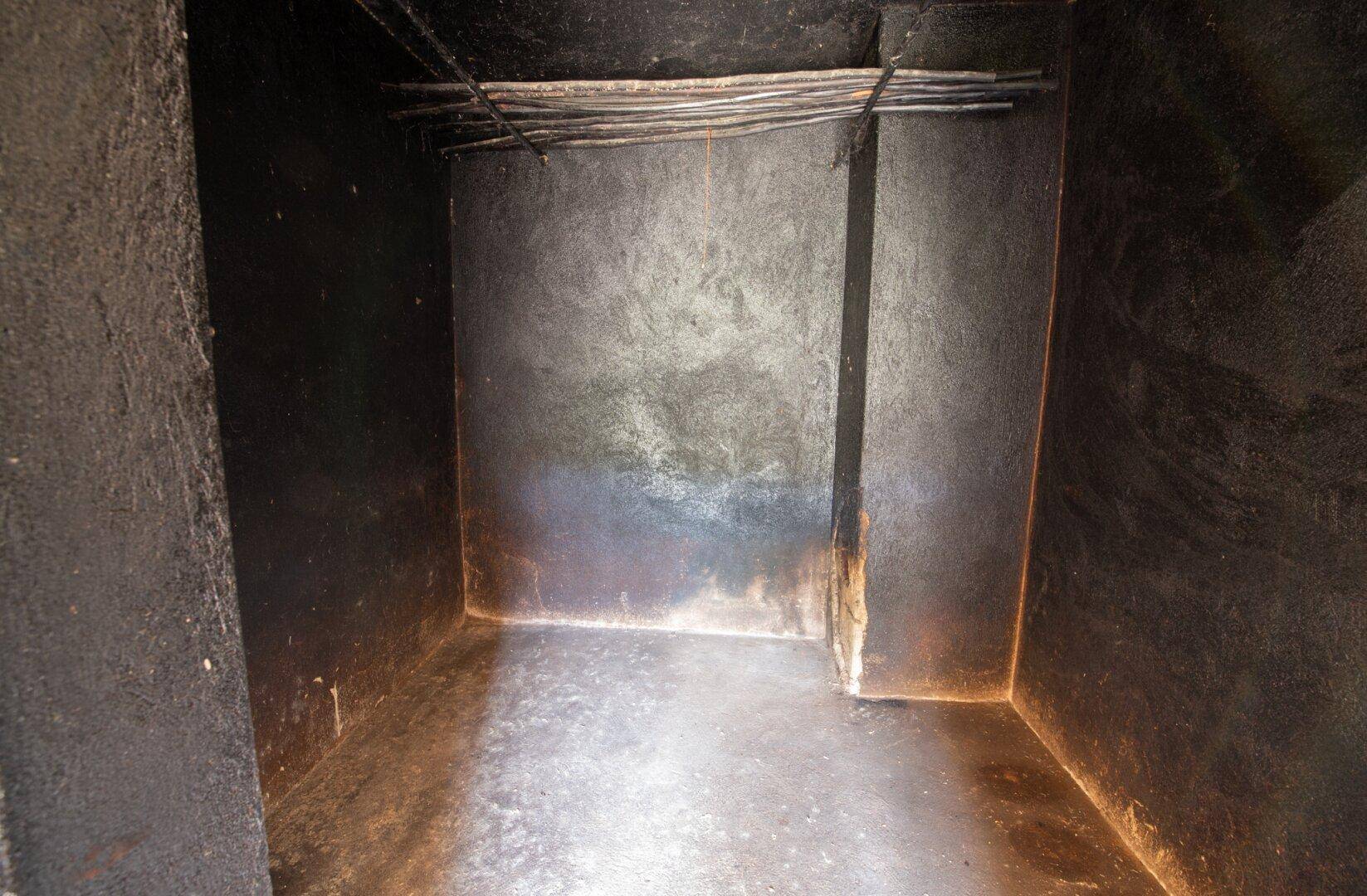Dunkler, enger Raum mit rauen Wänden und sichtbaren Kabeln, möglicherweise ein Abstellraum.