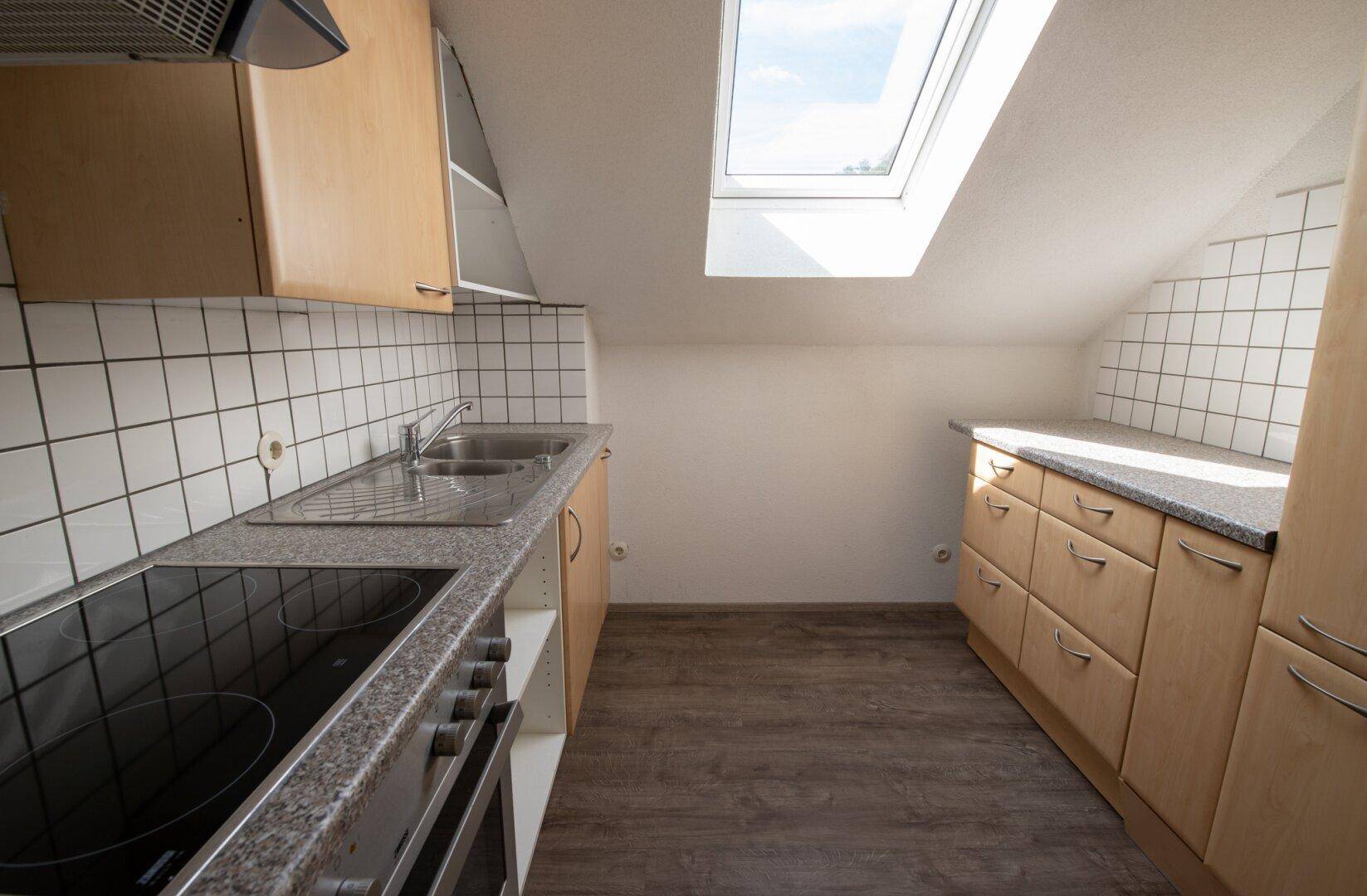 Dachgeschossküche mit Holzschränken, Granitarbeitsplatte und einem Dachfenster für Helligkeit.