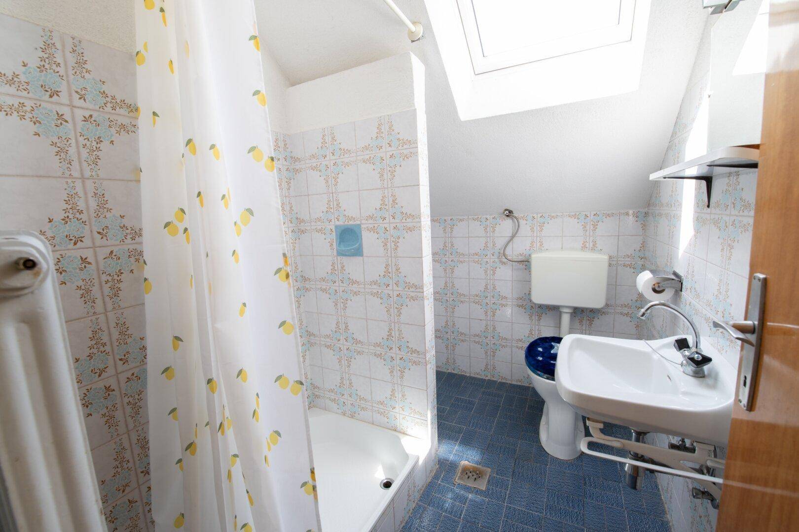 Dachgeschoss-Badezimmer mit Dusche, WC und Waschbecken unter einem Dachfenster.
