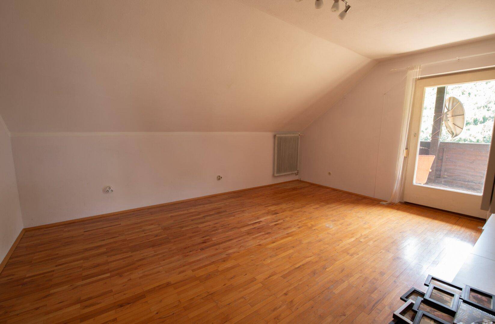 Geräumiges Dachgeschosszimmer mit Holzboden und Zugang zu einem Balkon.