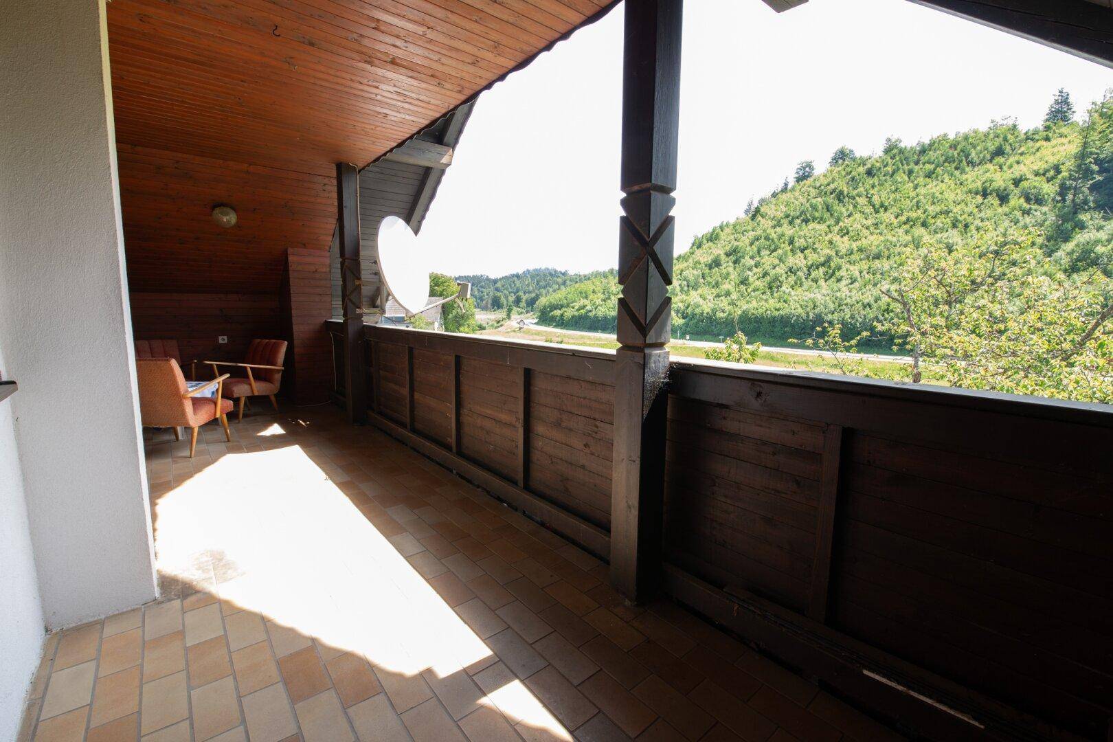 Überdachter Holzbalkon mit Fliesenboden und Sitzgelegenheiten, bietet Weitblick in die Landschaft.