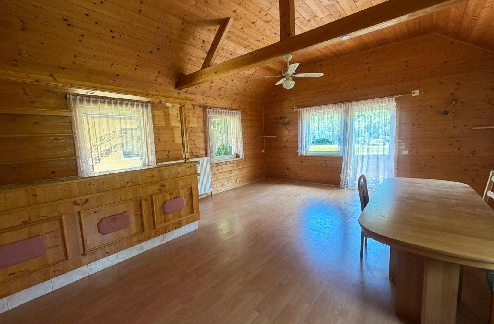 Geräumiger Wohn-Essbereich mit Holzvertäfelung, Deckenventilator und Blick ins Grüne.
