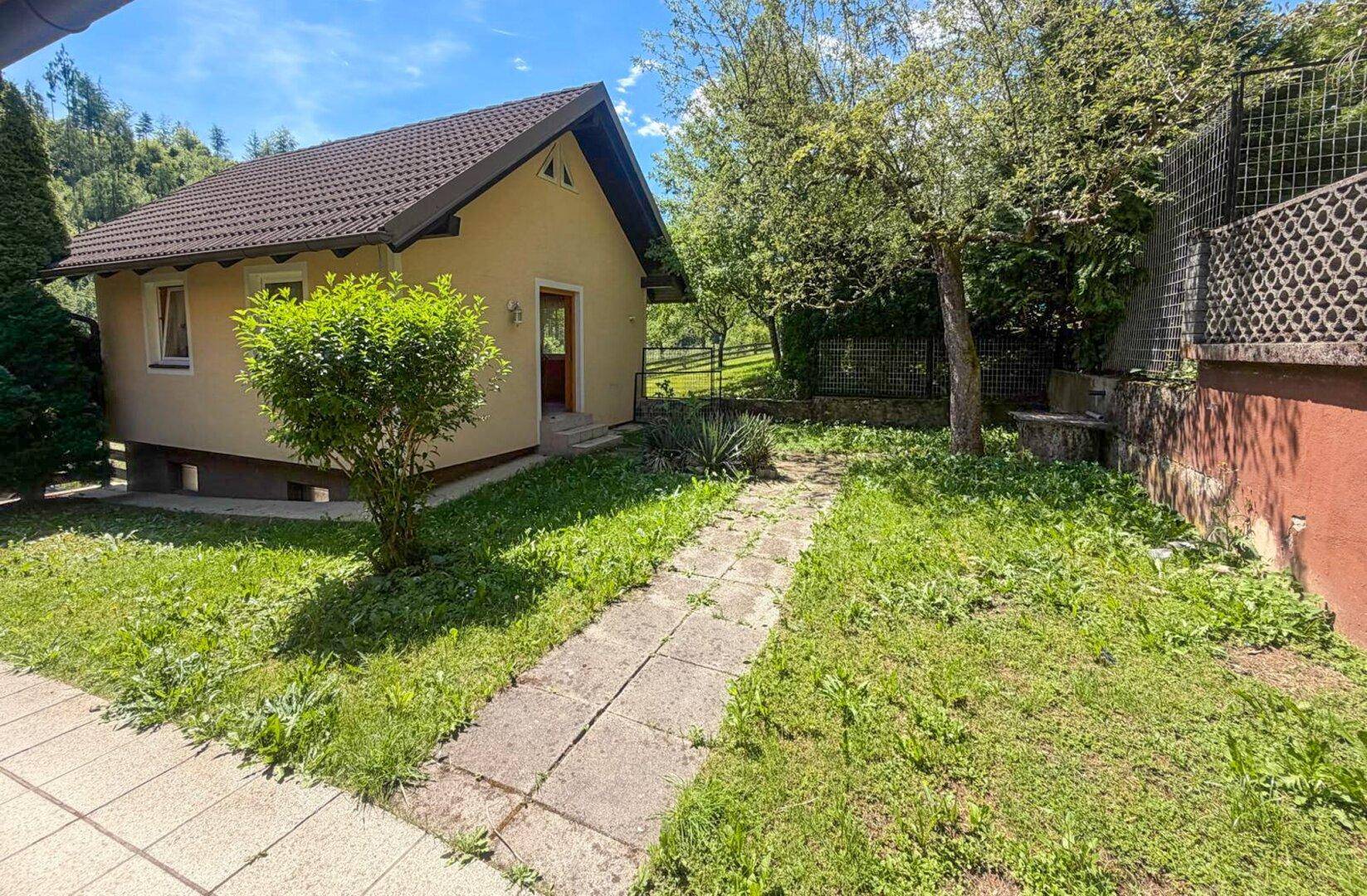 Gartenweg führt durch grüne Rasenfläche zu einem kleinen Nebengebäude in sonniger Lage.