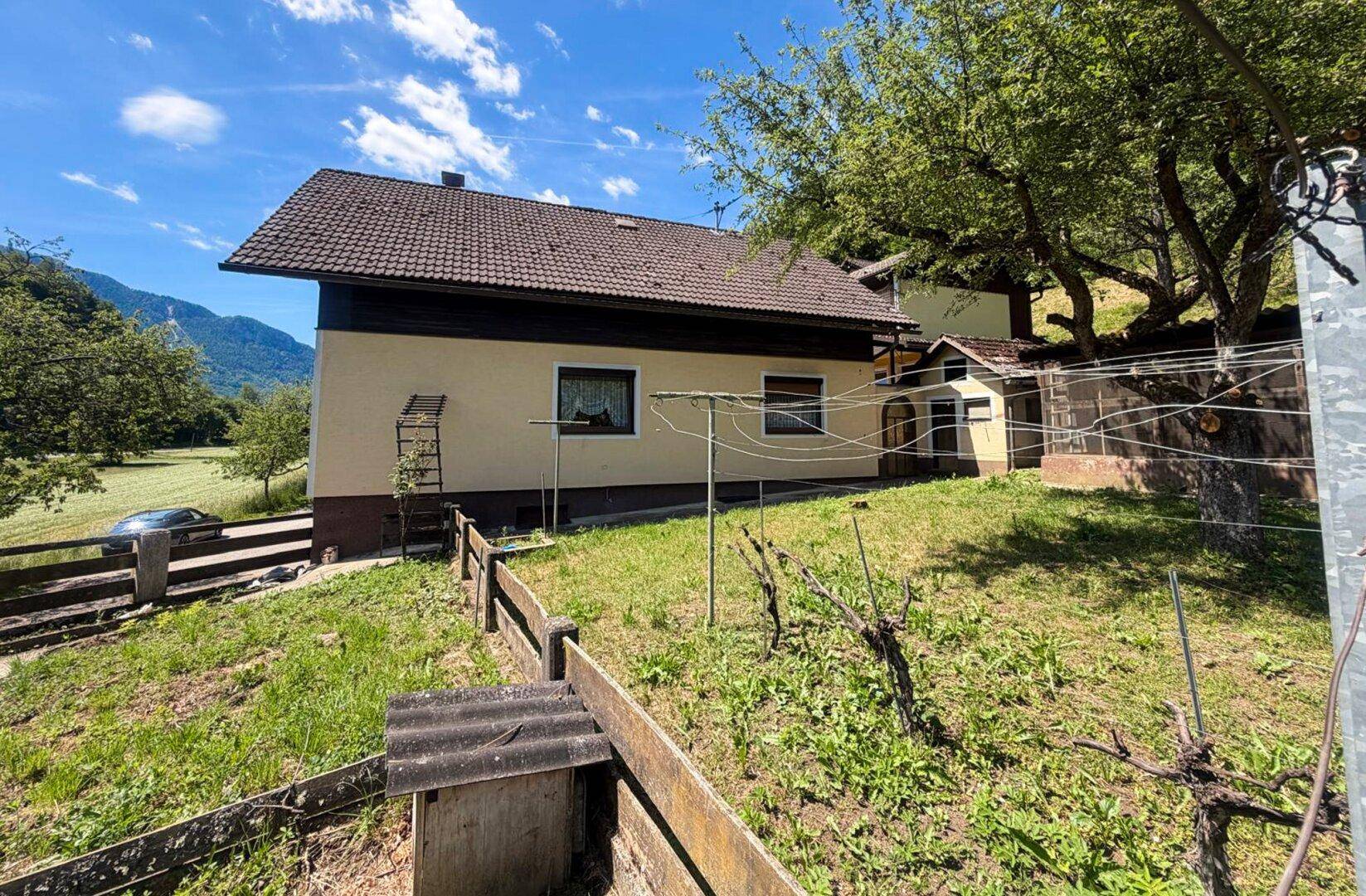 Seitenansicht des Hauses mit Wäscheleine im Garten und Blick auf die Berge und grüne Landschaft.