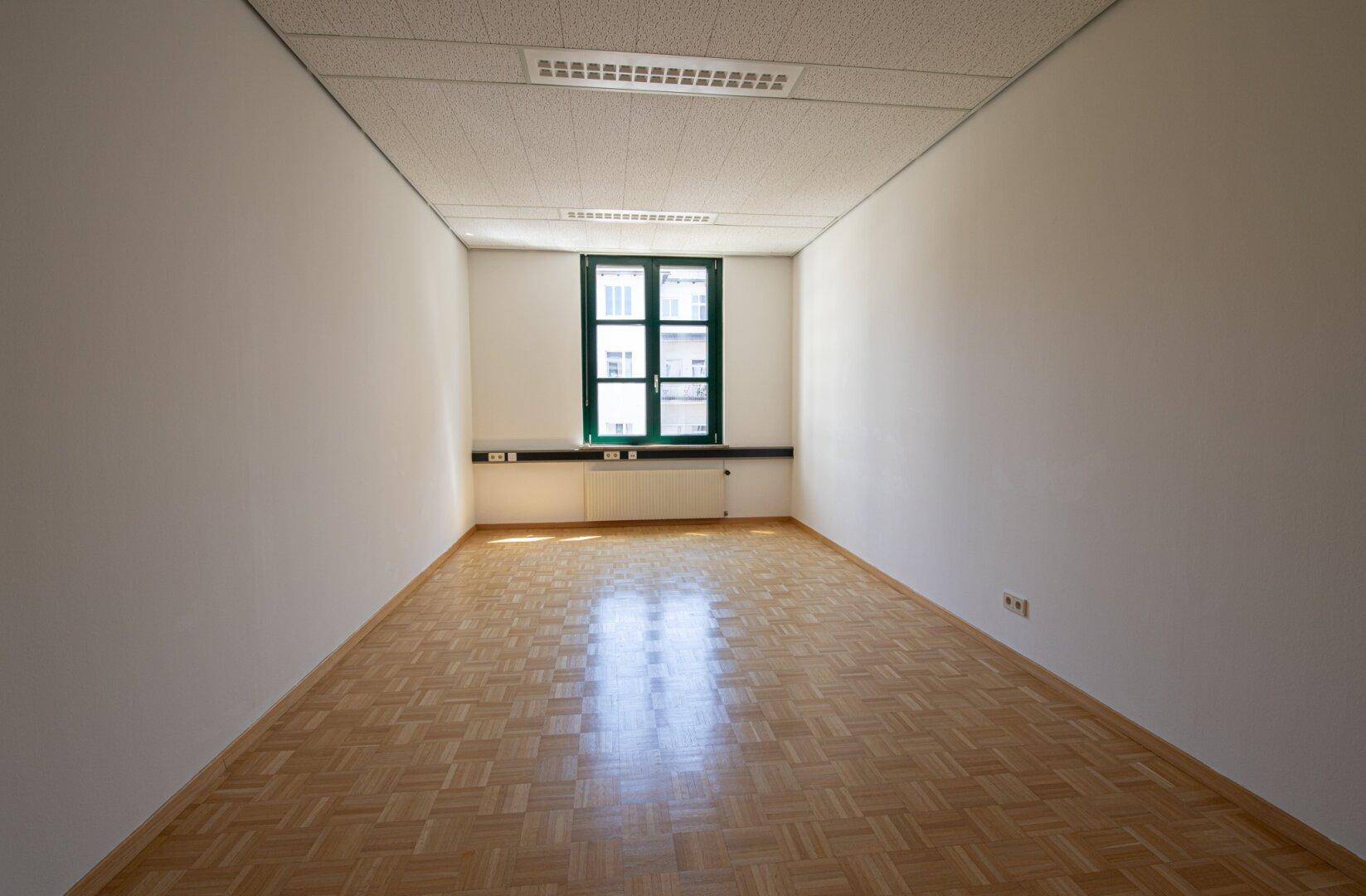 Langes, schmales Büro mit einem einzelnen Fenster und hellem Parkettboden, ideal für Einzelarbeitsplätze.