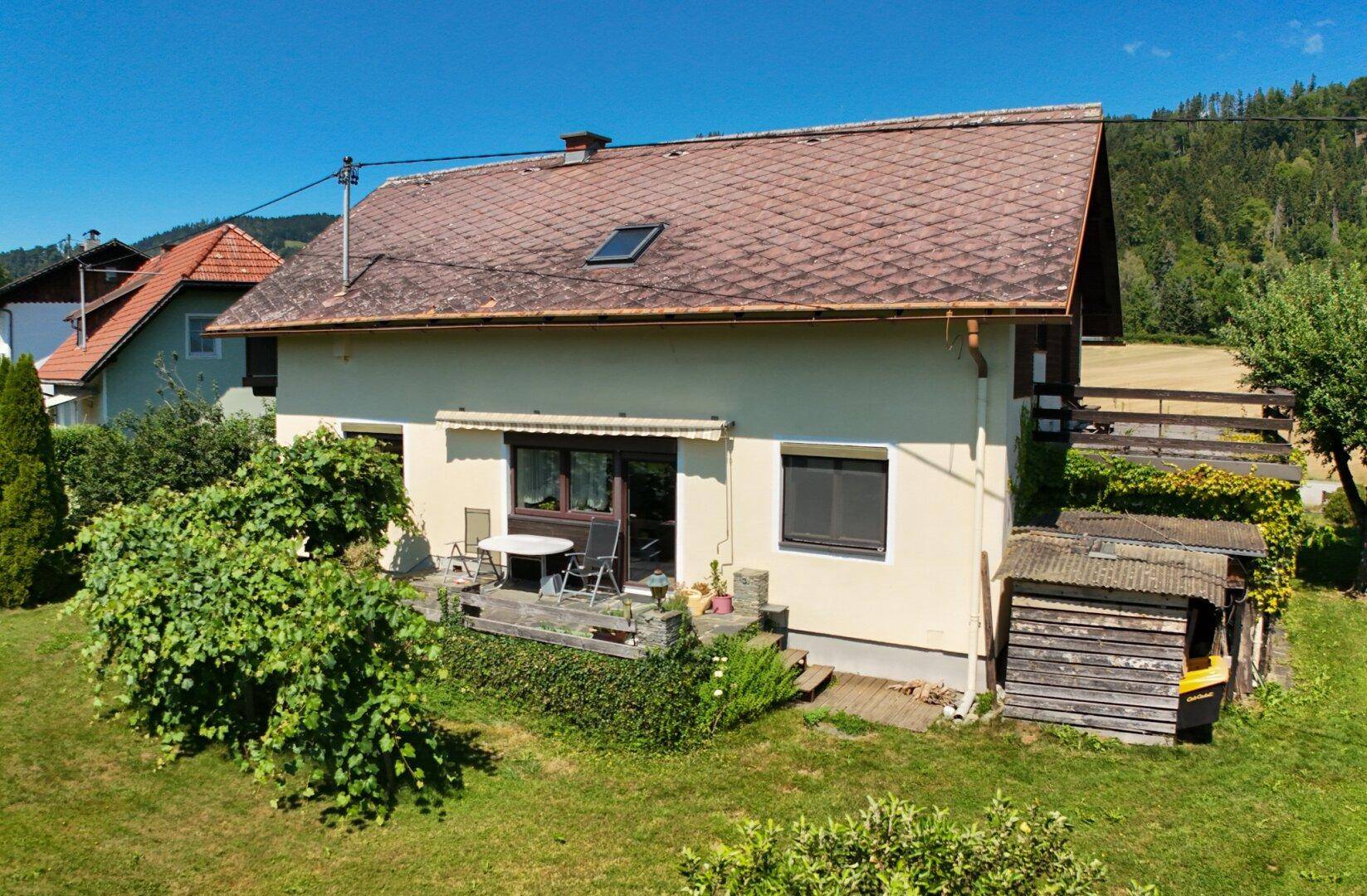 Rückseite des Hauses mit kleiner Terrasse, Gartenmöbeln und gepflegtem Rasen.