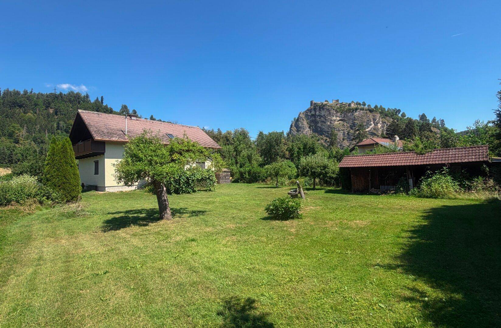 Weitläufiger Garten mit Rasen, Obstbäumen und beeindruckendem Blick auf die Felsen.