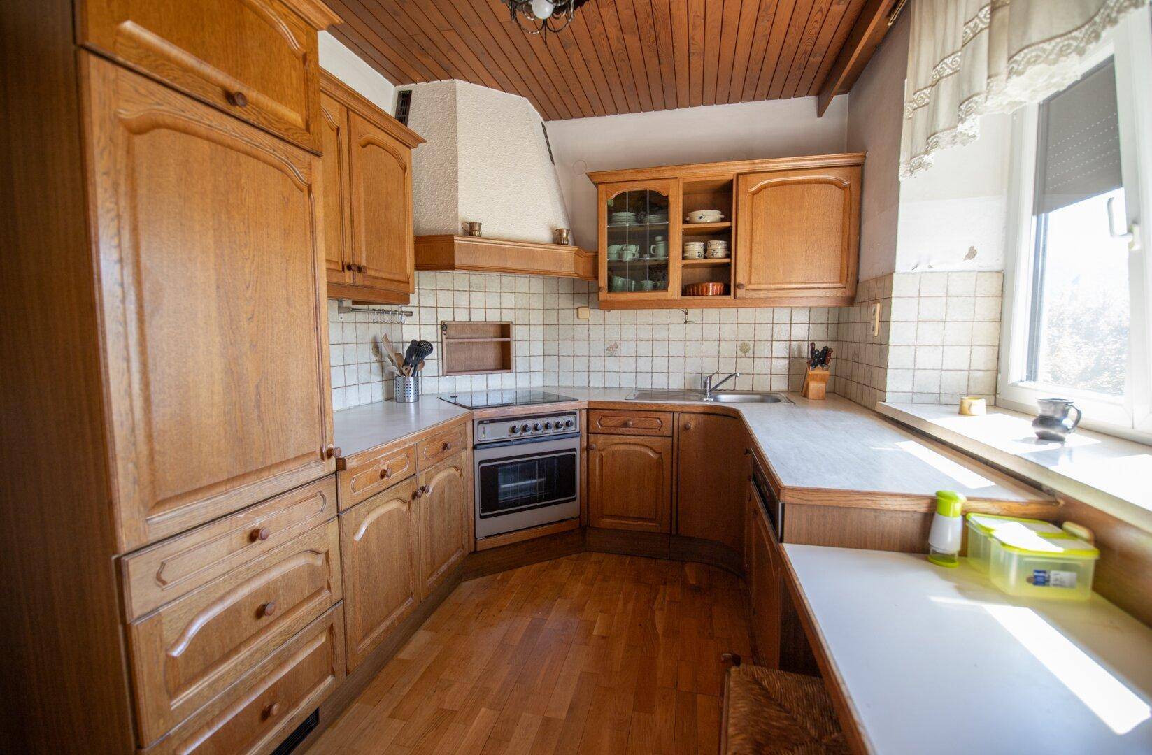 Traditionelle Holzküche mit Einbauschränken, Herd und Fenster mit viel Tageslicht.
