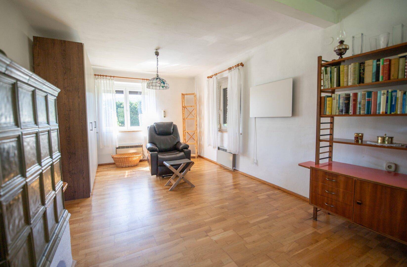 Helles Wohnzimmer mit Parkettboden, Kachelofen und gemütlichem Sessel.