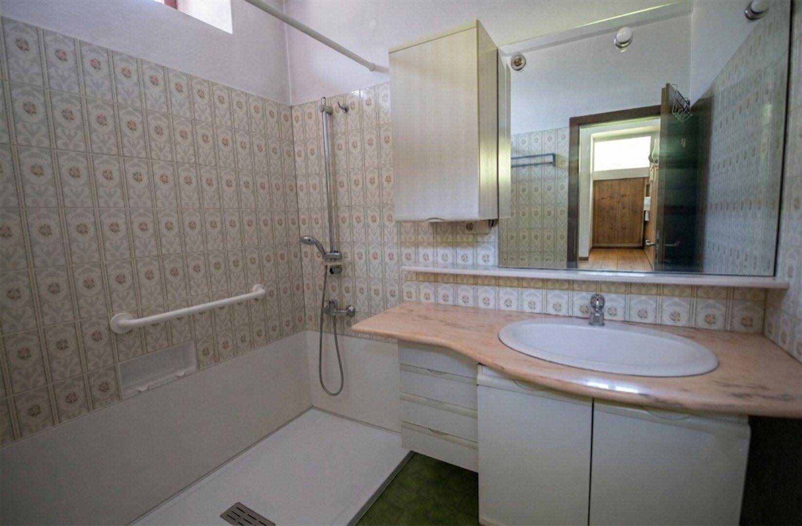 Badezimmer mit Dusche, Waschbecken und gemusterten Fliesen im 80er-Jahre-Stil.