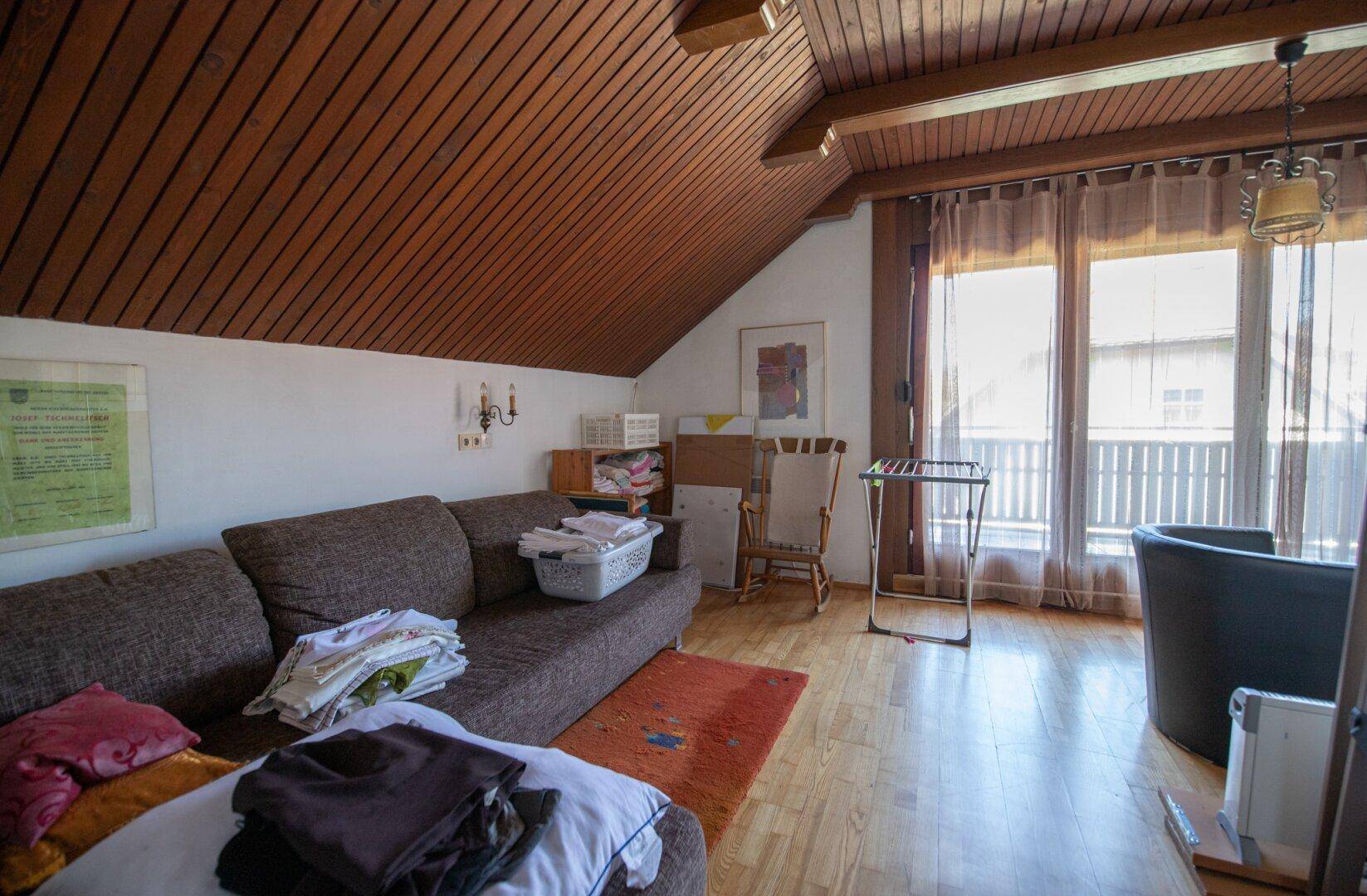 Dachgeschoss-Wohnraum mit Holzdecke, Holzbalken und Zugang zum Balkon.
