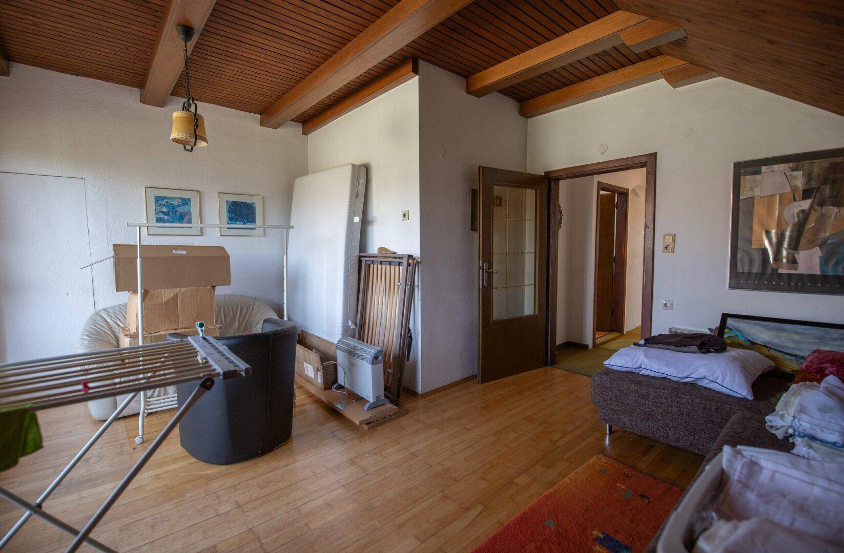 Dachgeschosszimmer mit Schrägen, Holzboden und Blick auf den Flur.