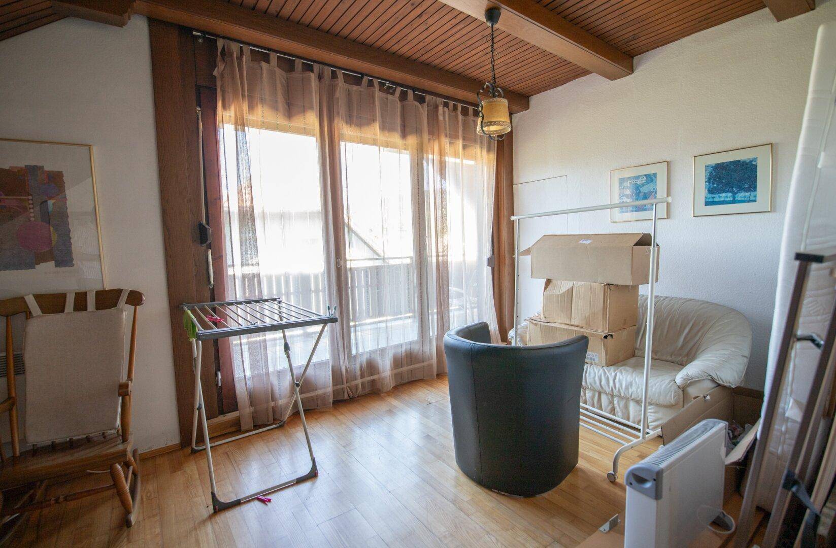 Helles Dachgeschosszimmer mit großen Fenstern und Zugang zum Balkon.