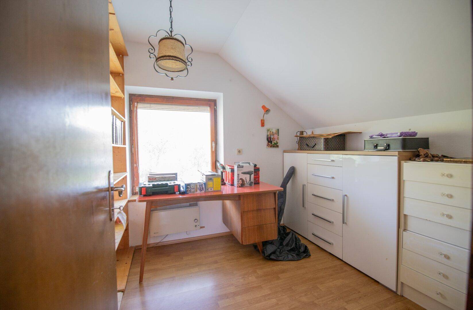 Arbeitszimmer im Dachgeschoss mit Schreibtisch, Schränken und Fenster.
