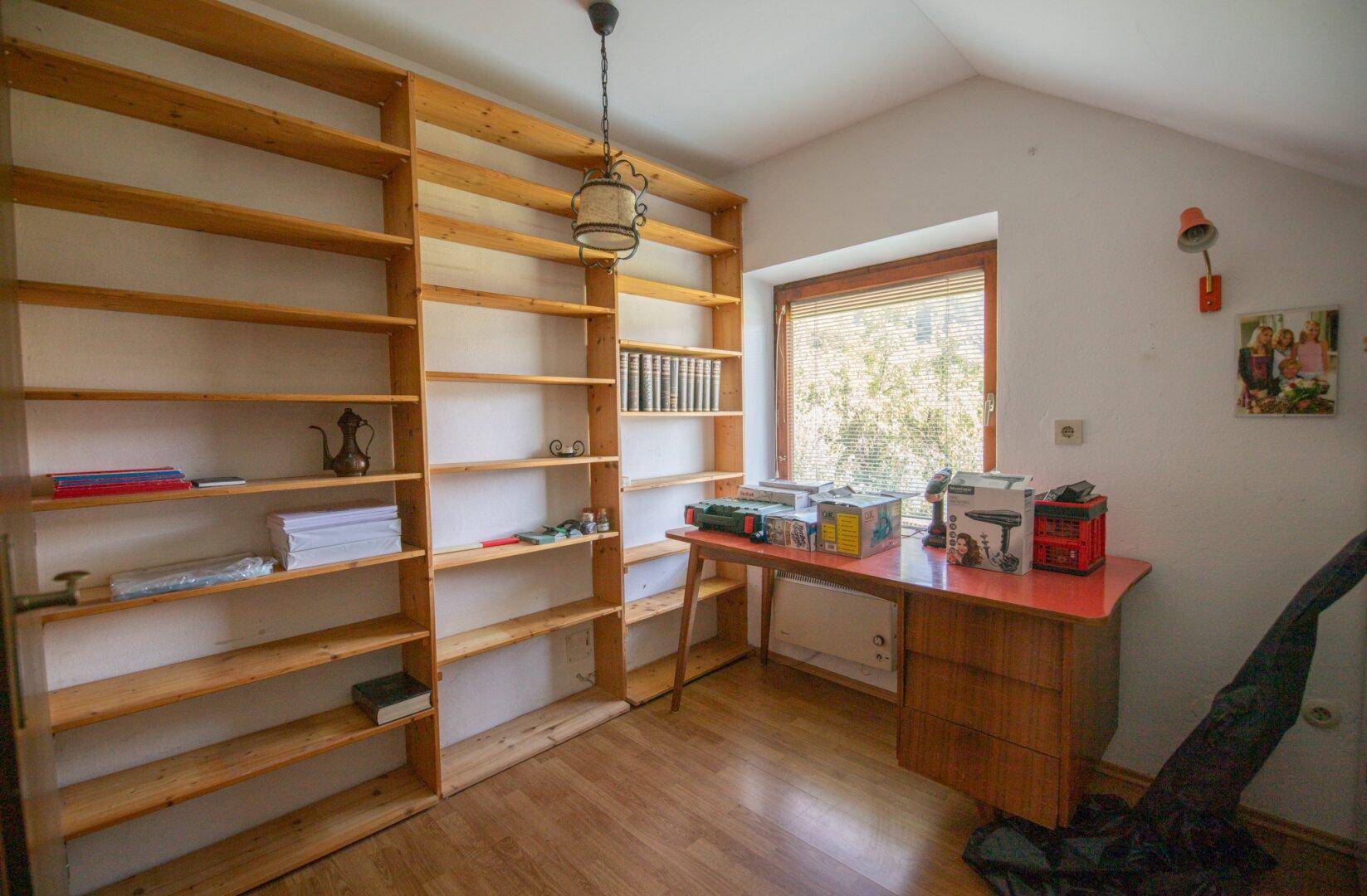 Arbeitszimmer mit Bücherregalen, Schreibtisch und Fenster im Dachgeschoss.