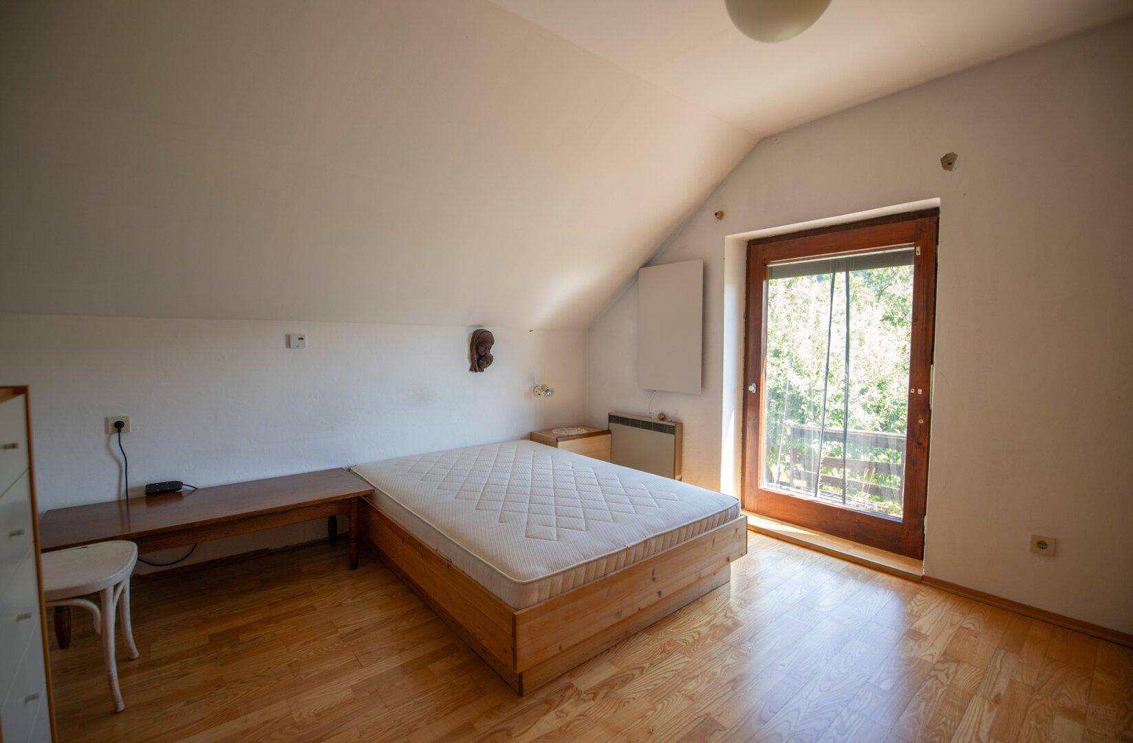 Schlafzimmer im Dachgeschoss mit Bett, Holzboden und Balkonzugang.