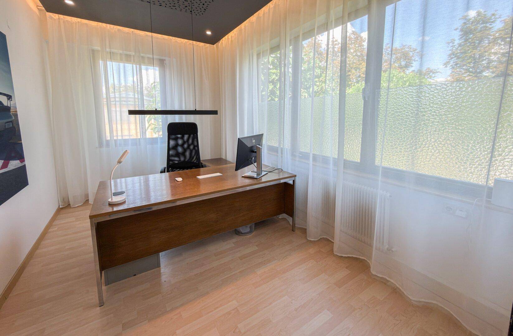 Modernes Büro mit Holztisch, ergonomischem Stuhl und großen Fenstern, die viel Tageslicht hereinlassen.