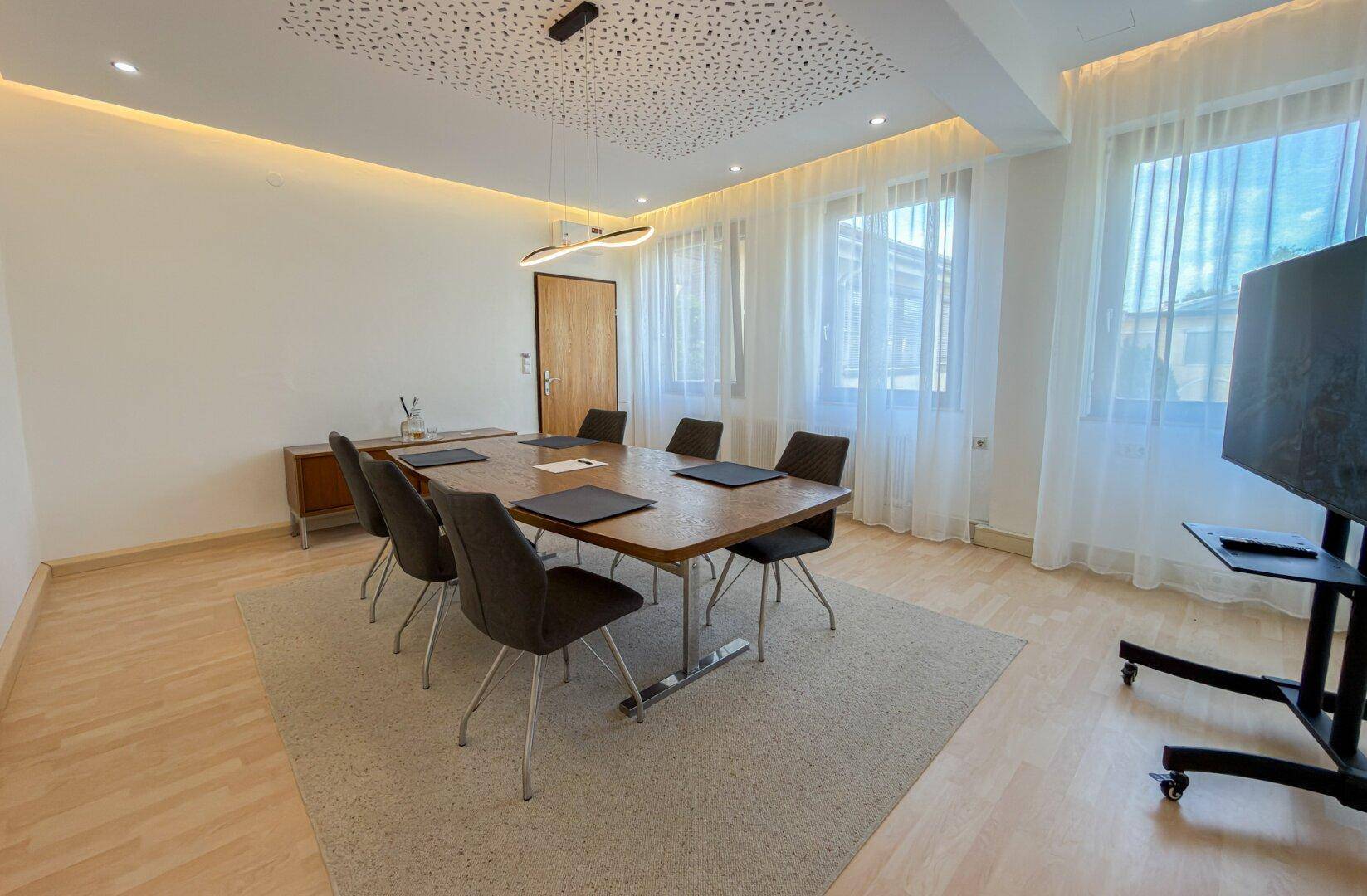 Geräumiger Konferenzraum mit modernem Holztisch, bequemen Stühlen und indirekter Deckenbeleuchtung.